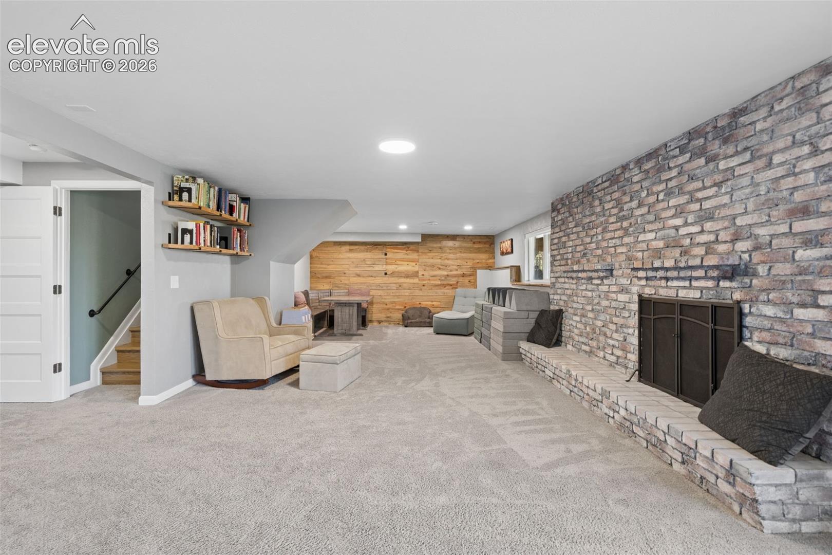 Basement Expansive living area featuring a full-height brick fireplace hearth, wood-paneled accent wall, neutral carpeting, and built-in wall shelving