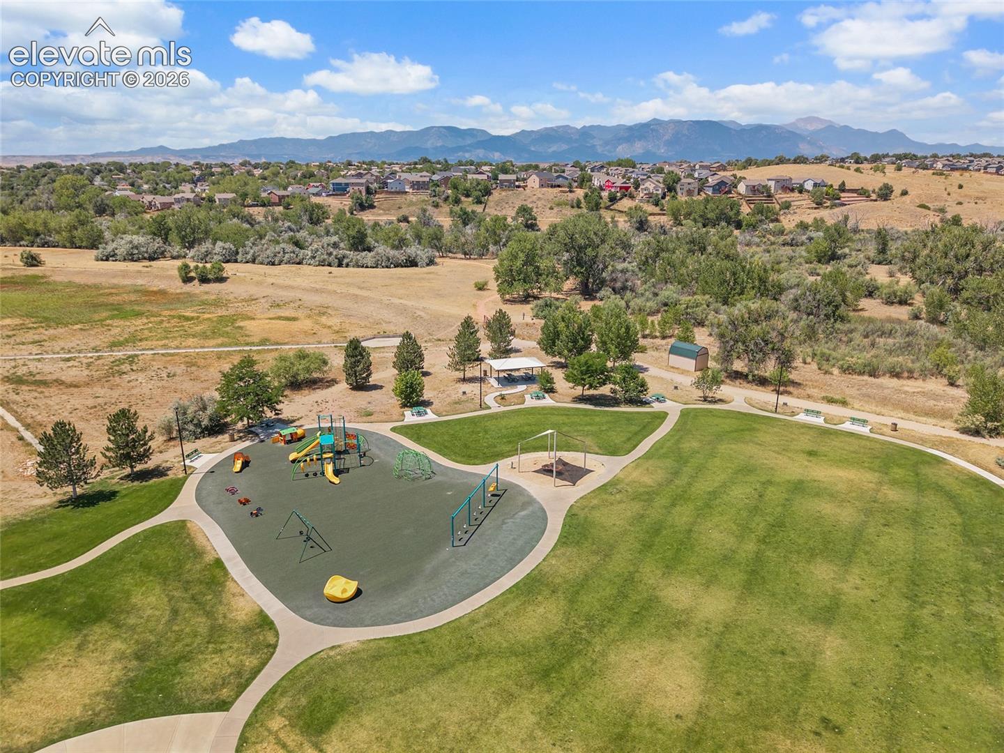 Public park featuring expansive manicured lawns, playground equipment, concrete walking paths, and mountain scenery