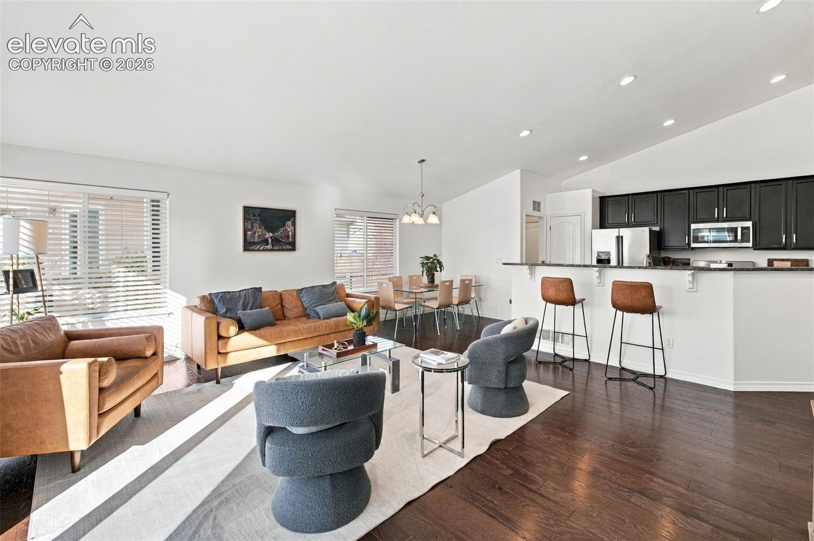 Open-concept interior featuring vaulted ceilings, recessed lighting, dark cabinetry, a breakfast bar, and wood-finish flooring