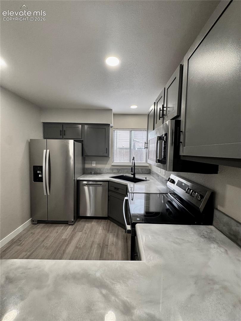 Updated kitchen featuring wood-finish flooring, stainless steel appliances, dark cabinetry, and light-toned countertops