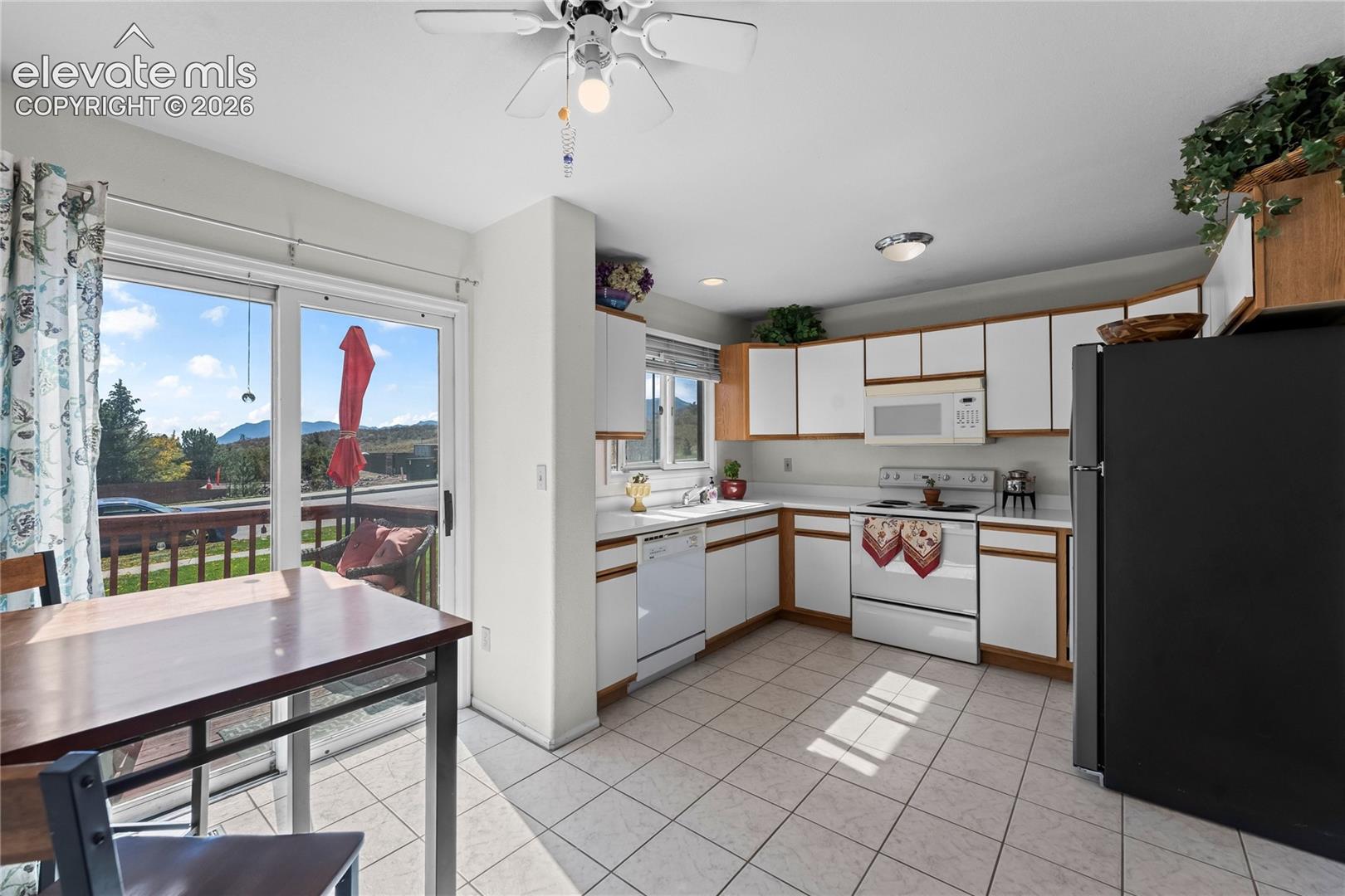 Kitchen featuring L-shaped cabinetry with white doors, tile flooring, and white appliances