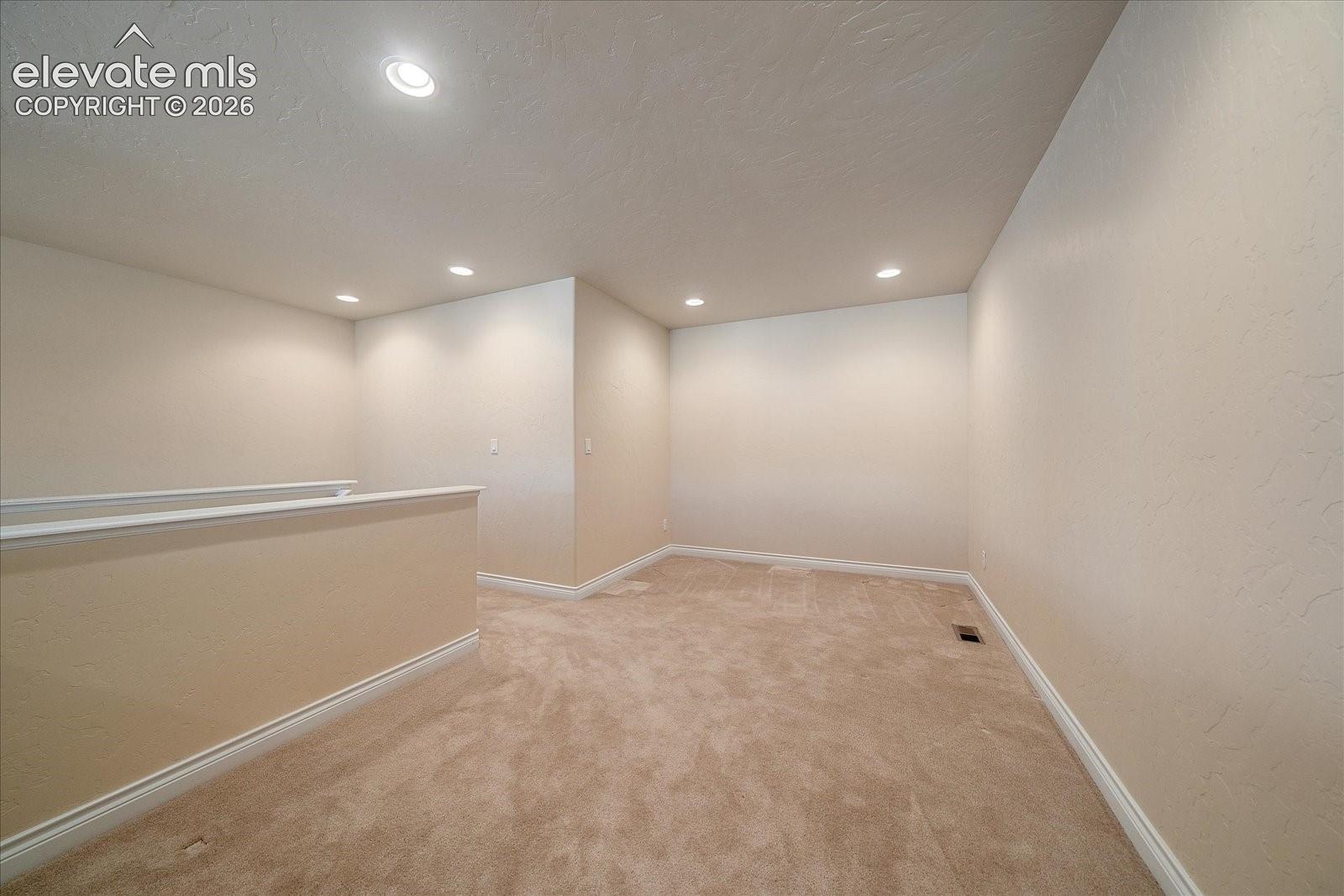 Neutral-toned interior space featuring textured walls, wall-to-wall carpeting, and recessed ceiling lighting