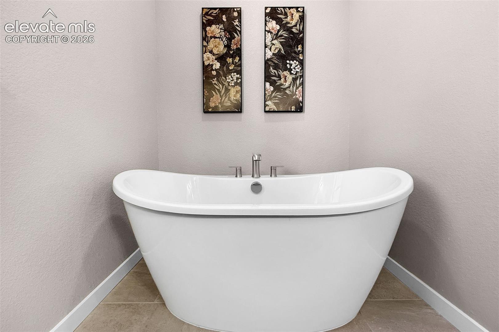 Freestanding soaking tub with a deck-mounted faucet and tiled flooring
