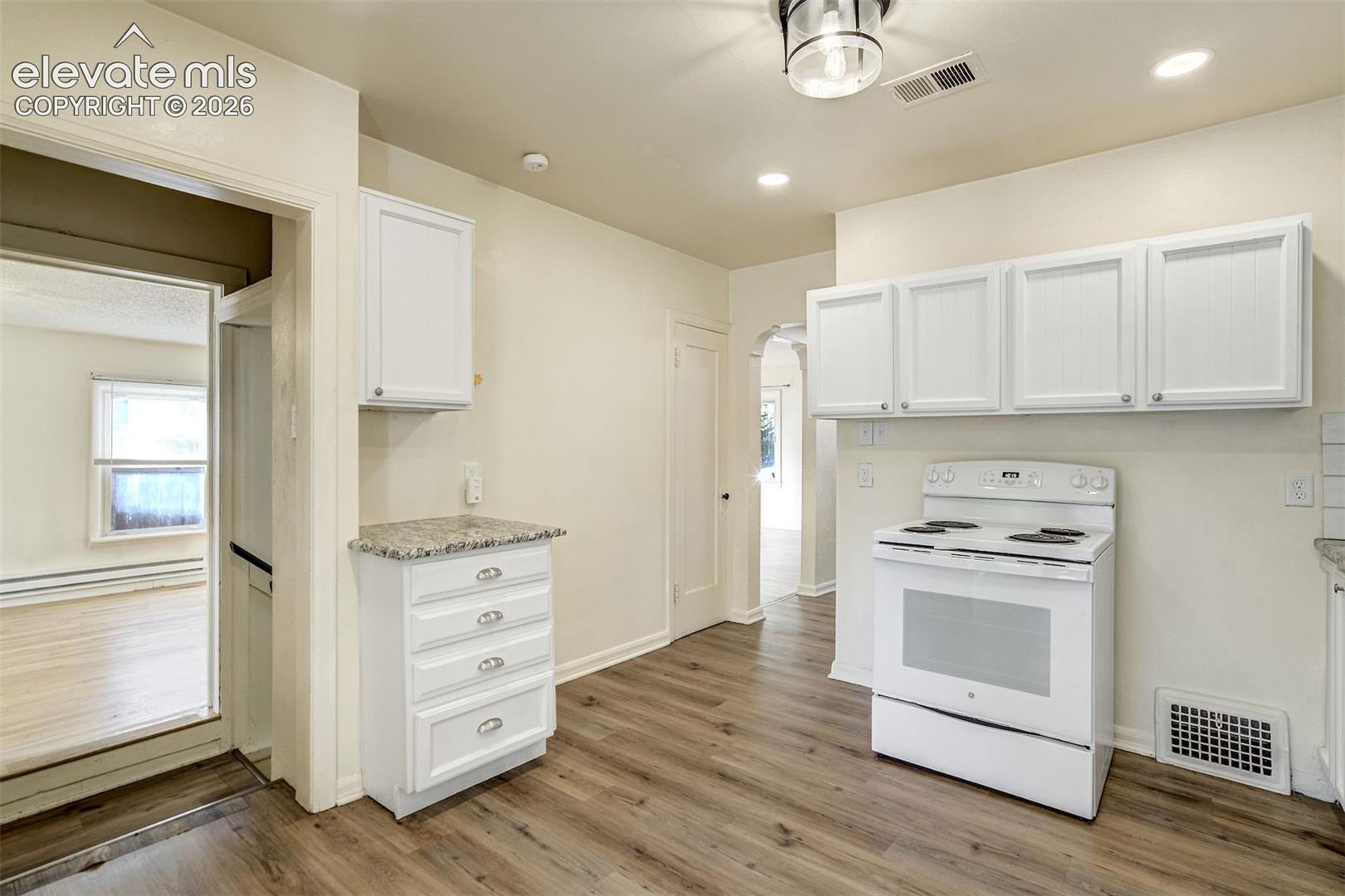 Kitchen featuring white cabinetry, stone-surface countertops, wood-finish flooring, and a white electric range