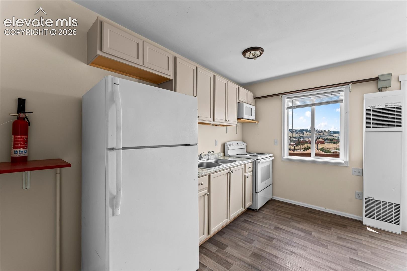 Kitchen featuring wood-finish flooring, white appliances, light-toned cabinetry, and a window with a distant landscape