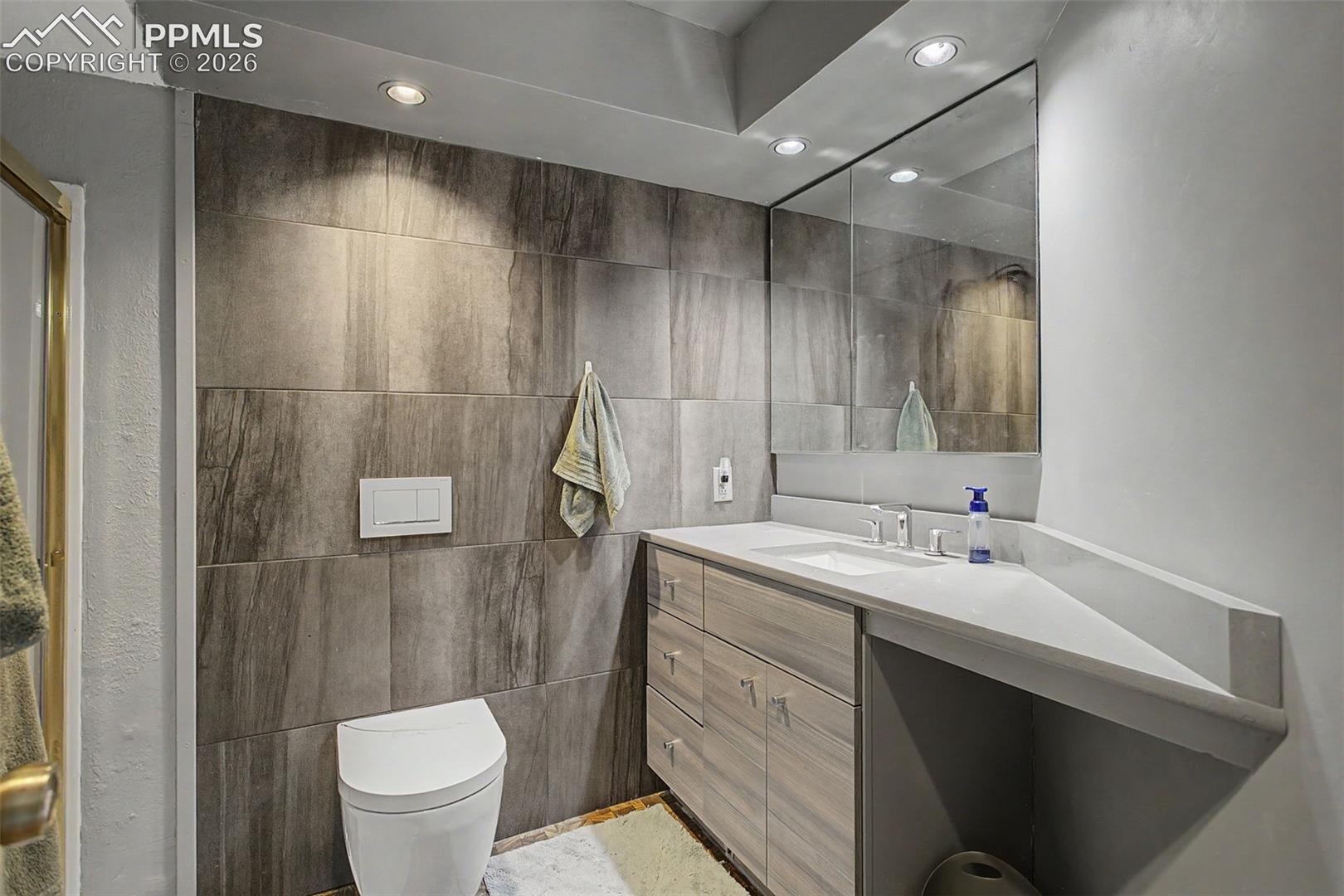 Basement 3/4 bathroom, floor-to-ceiling tiled accent wall and walk-in shower with glass door.