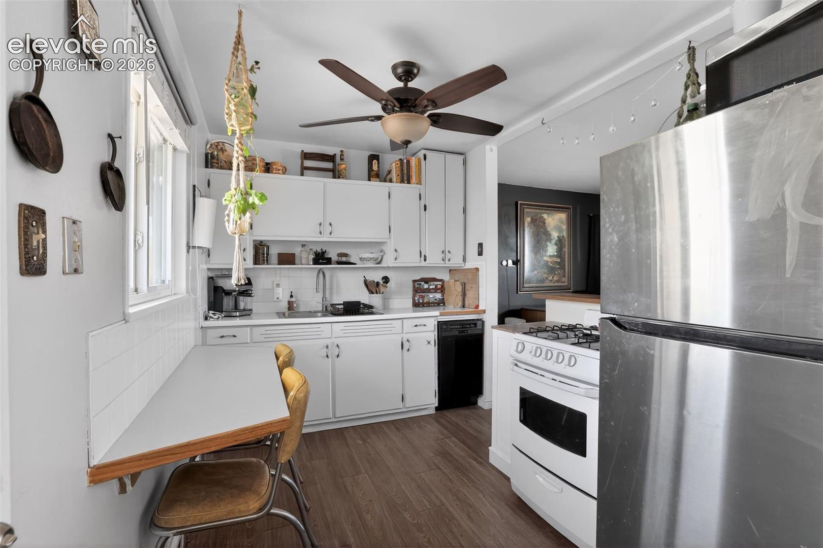 Kitchen featuring white cabinetry, wood-finish flooring, a stainless-steel refrigerator, a white range, and a ceiling fan with integrated lighting
