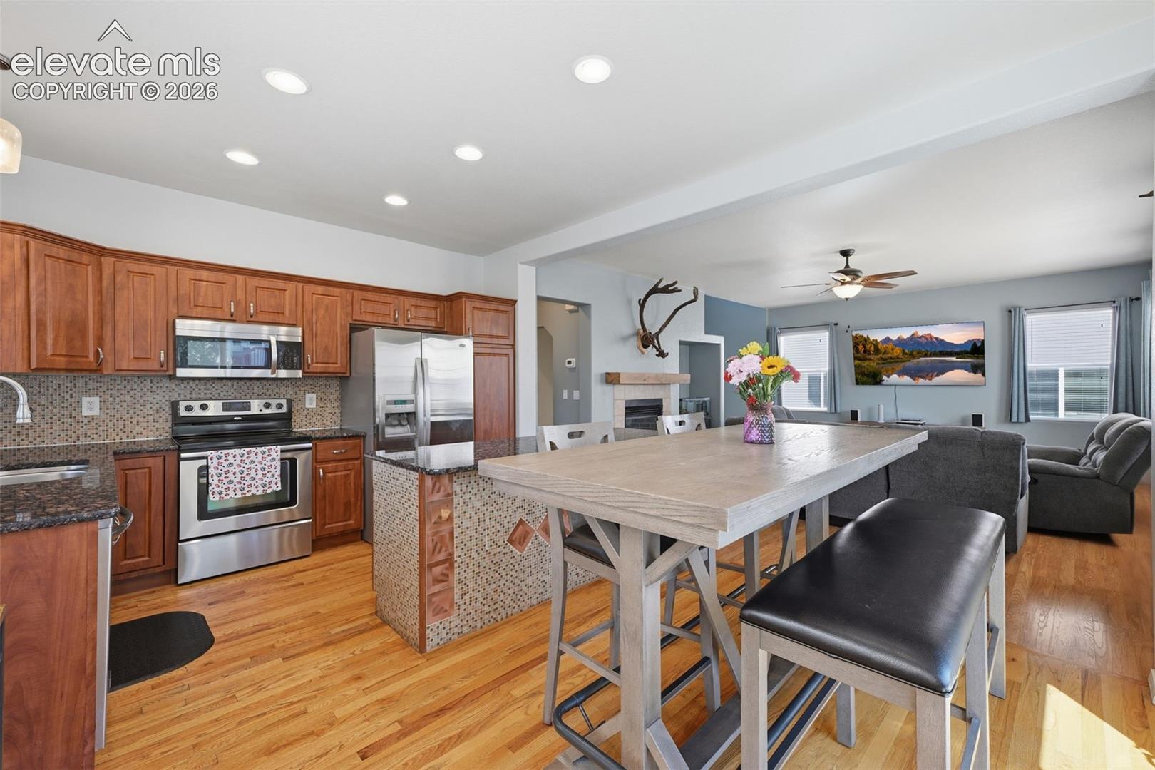 Wood-finish flooring throughout, with a kitchen featuring wood cabinetry, stainless steel appliances, and a tiled backsplash