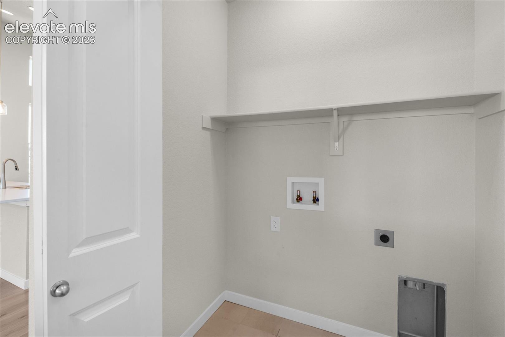 Utility area featuring wood-finish flooring, a wall-mounted shelf, and dedicated water and electrical hookups