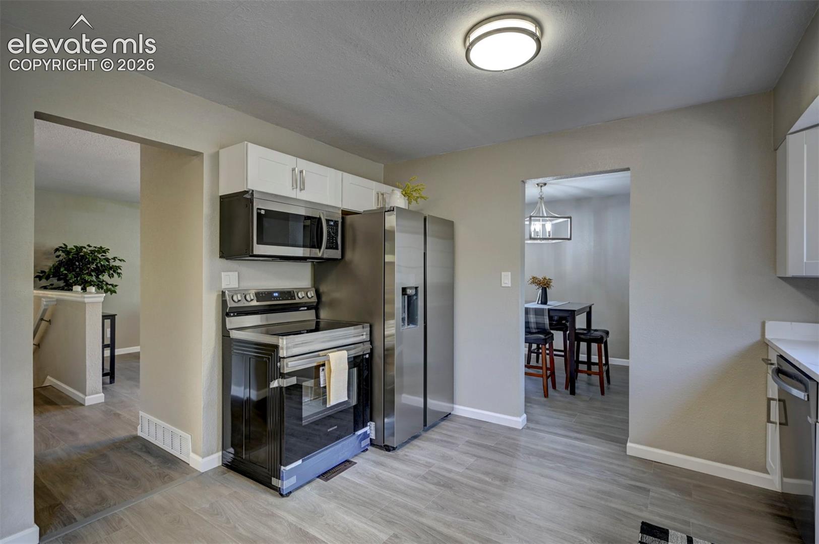 Kitchen featuring stainless steel appliances, wood-finish flooring, white upper cabinetry, and a flush-mount ceiling light