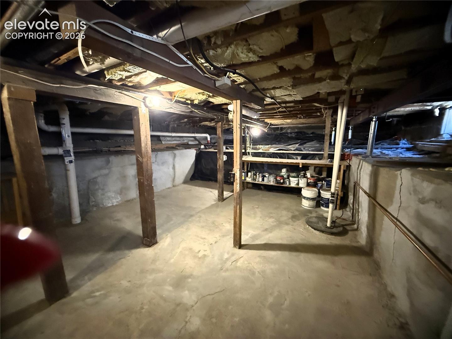 Unfinished crawl space featuring concrete foundation walls, concrete floor, vertical wood support posts, and exposed ceiling joists with insulation