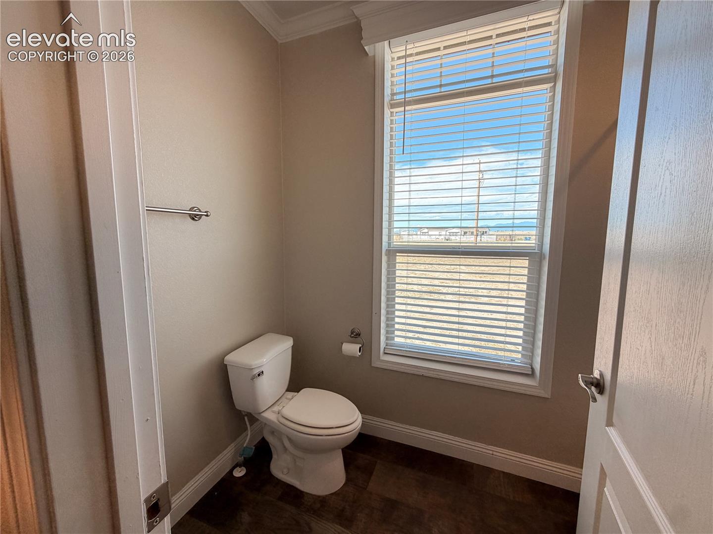 Bathroom featuring a tall window with horizontal blinds, neutral wall paint, dark-toned flooring, and a chrome towel bar