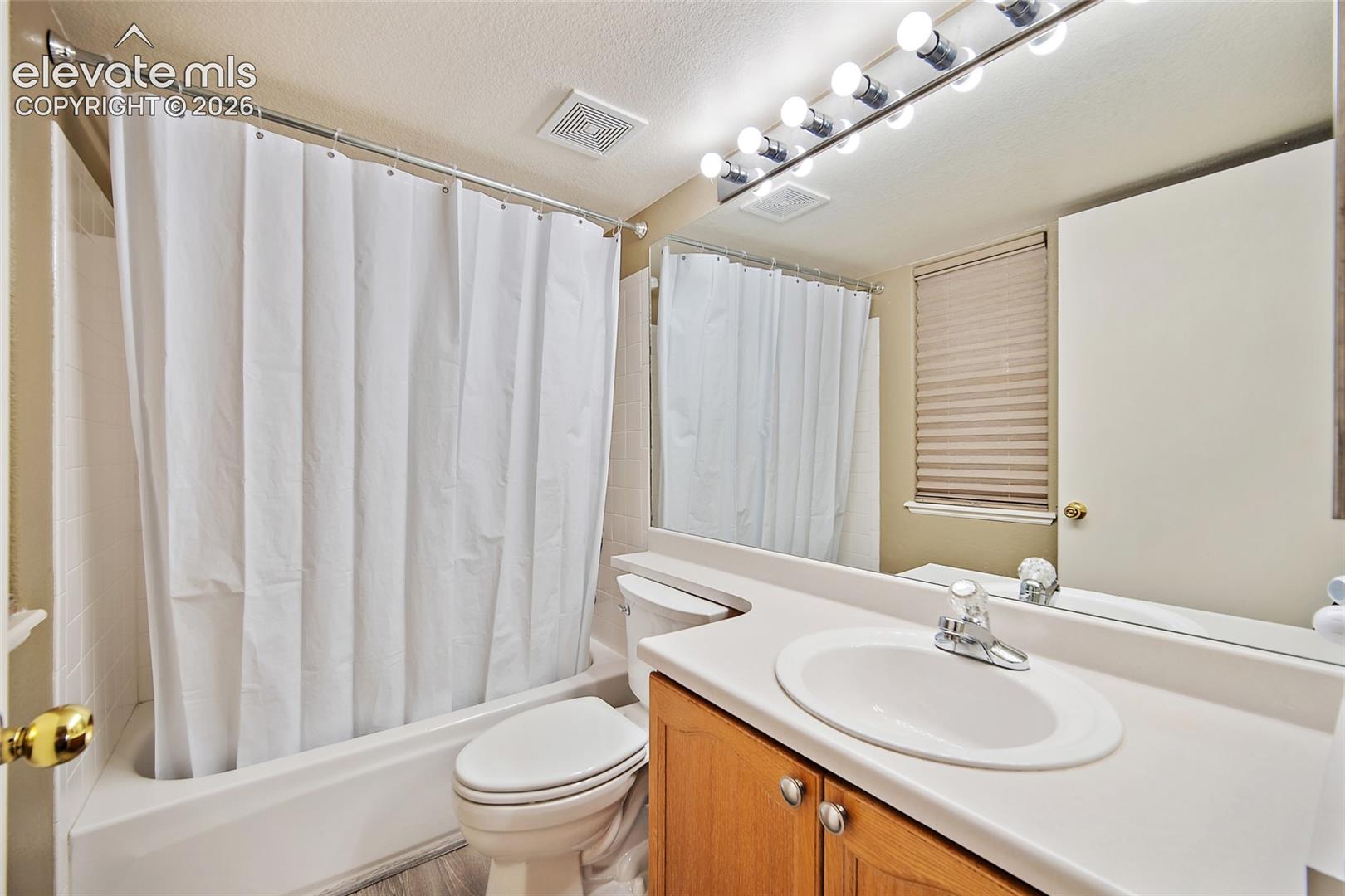 Full bathroom featuring an integrated tub and shower, a single vanity with a white countertop, and a wood-finish cabinet