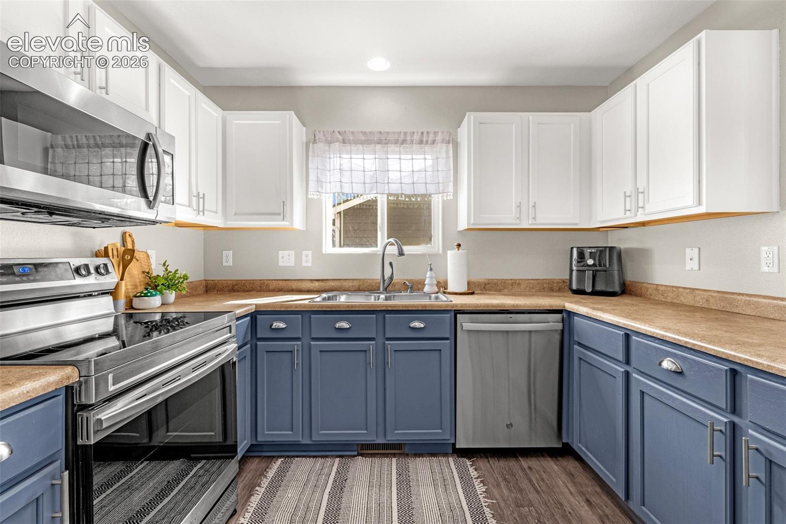 Kitchen featuring two-tone cabinetry, stainless steel appliances, laminate countertops, and wood-finish flooring
