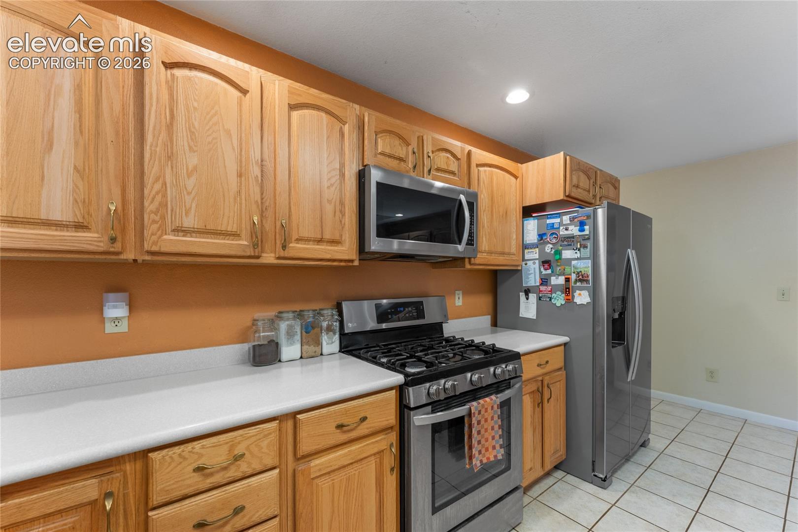 Kitchen featuring light wood cabinetry, stainless steel appliances, white countertops, and tiled flooring