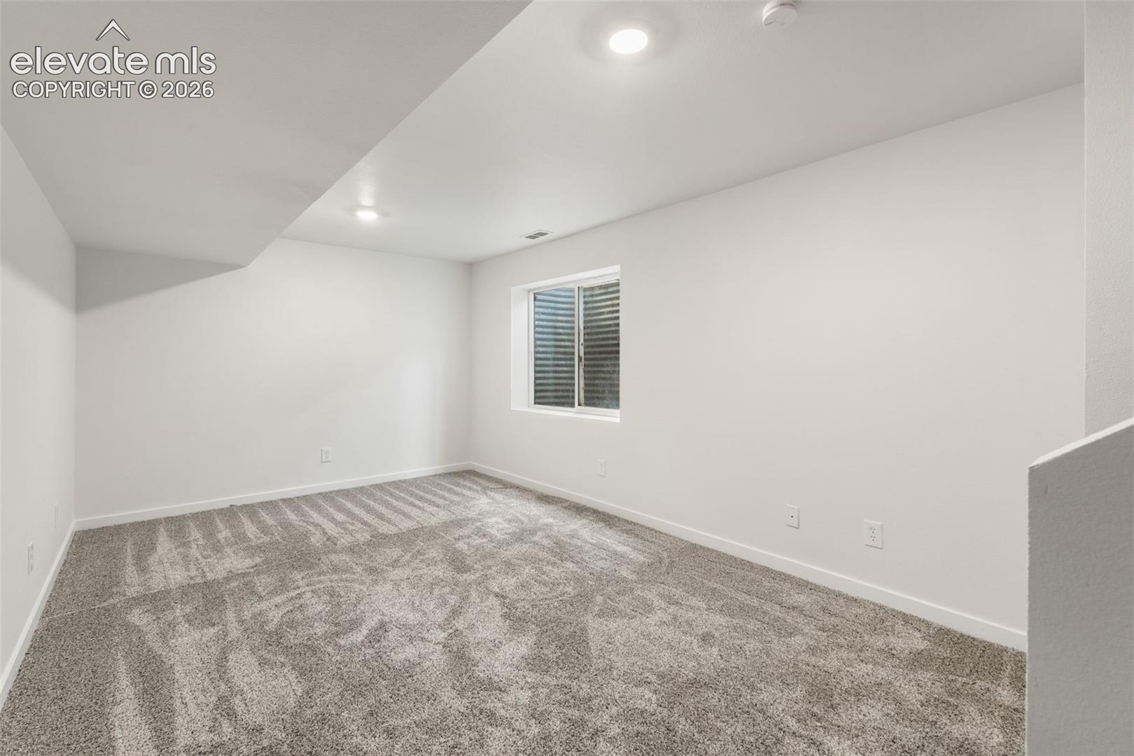 Neutral-toned carpeting, recessed ceiling lighting, and a window with a window well cover