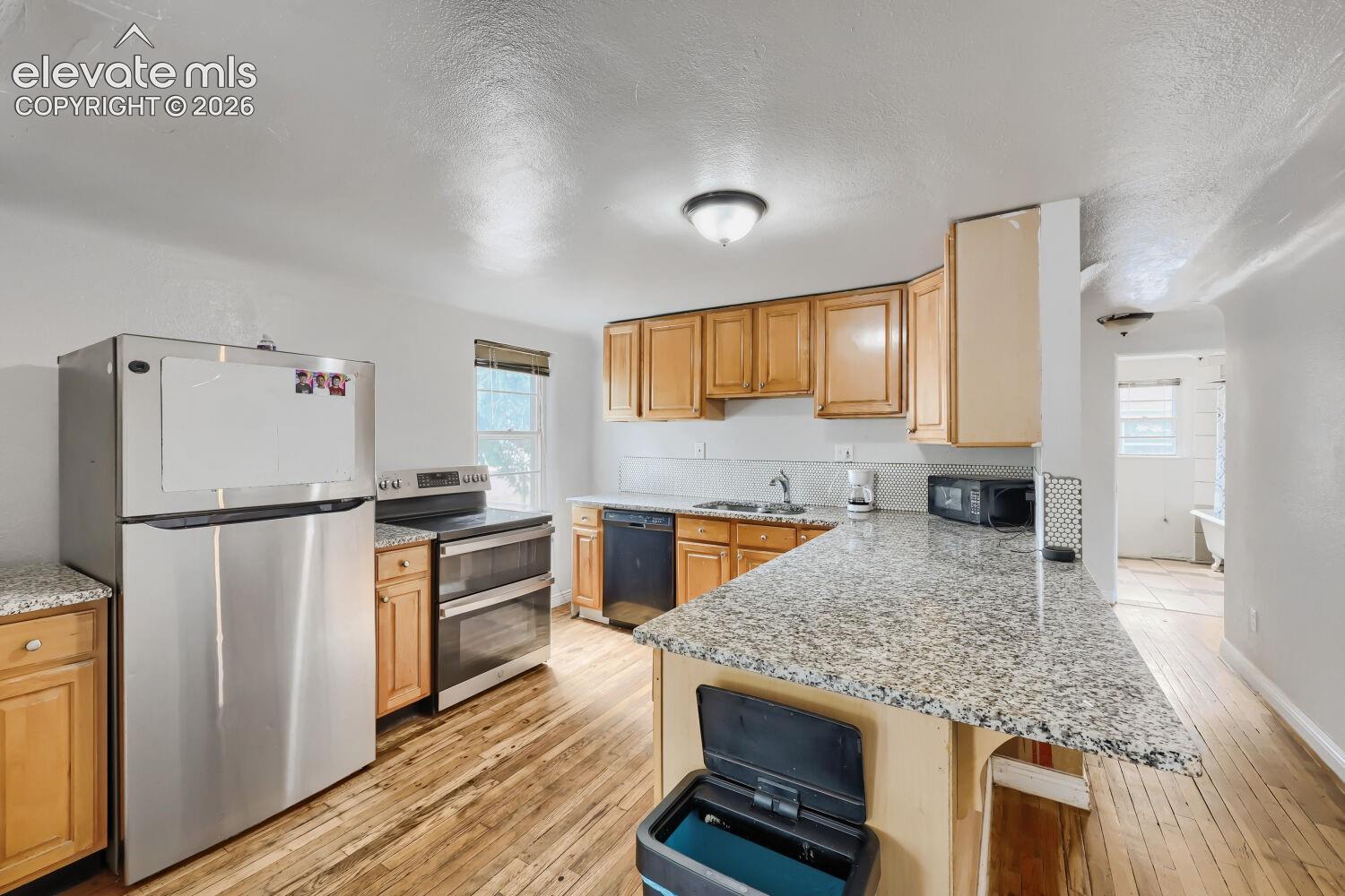 Kitchen featuring stainless steel appliances, wood-finish flooring, light wood cabinetry, and granite-style countertops