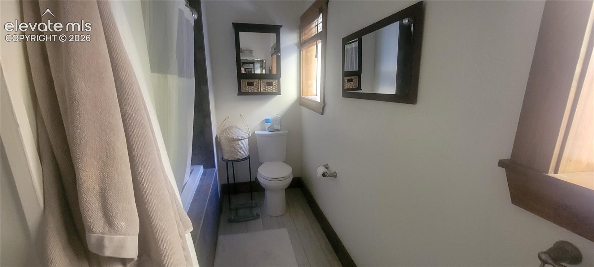 Bathroom featuring a built-in tub with shower, wood-finish flooring, and a window with wood-finish trim