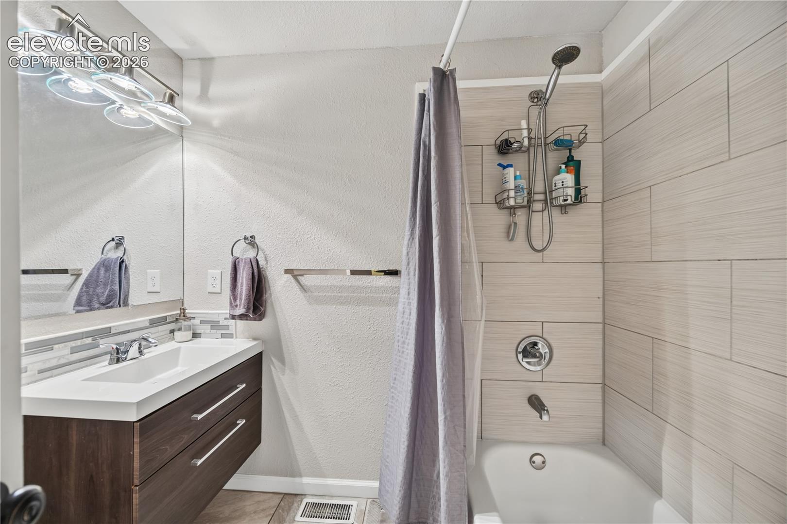 Bathroom featuring a floating vanity with dual drawers, rectangular sink, full-width vanity mirror, and horizontal tile shower surround with a handheld shower head fixture