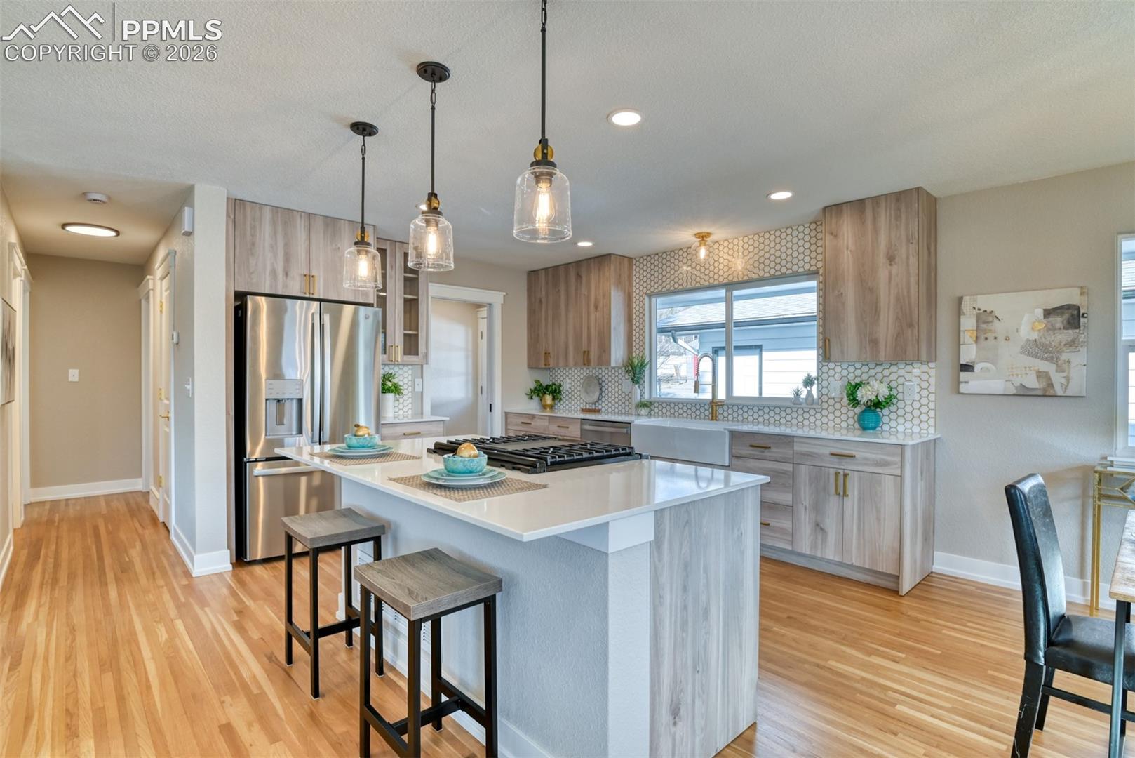 Kitchen featuring stainless steel appliances, a breakfast bar, decorative light fixtures, glass insert cabinets, and light stone countertops