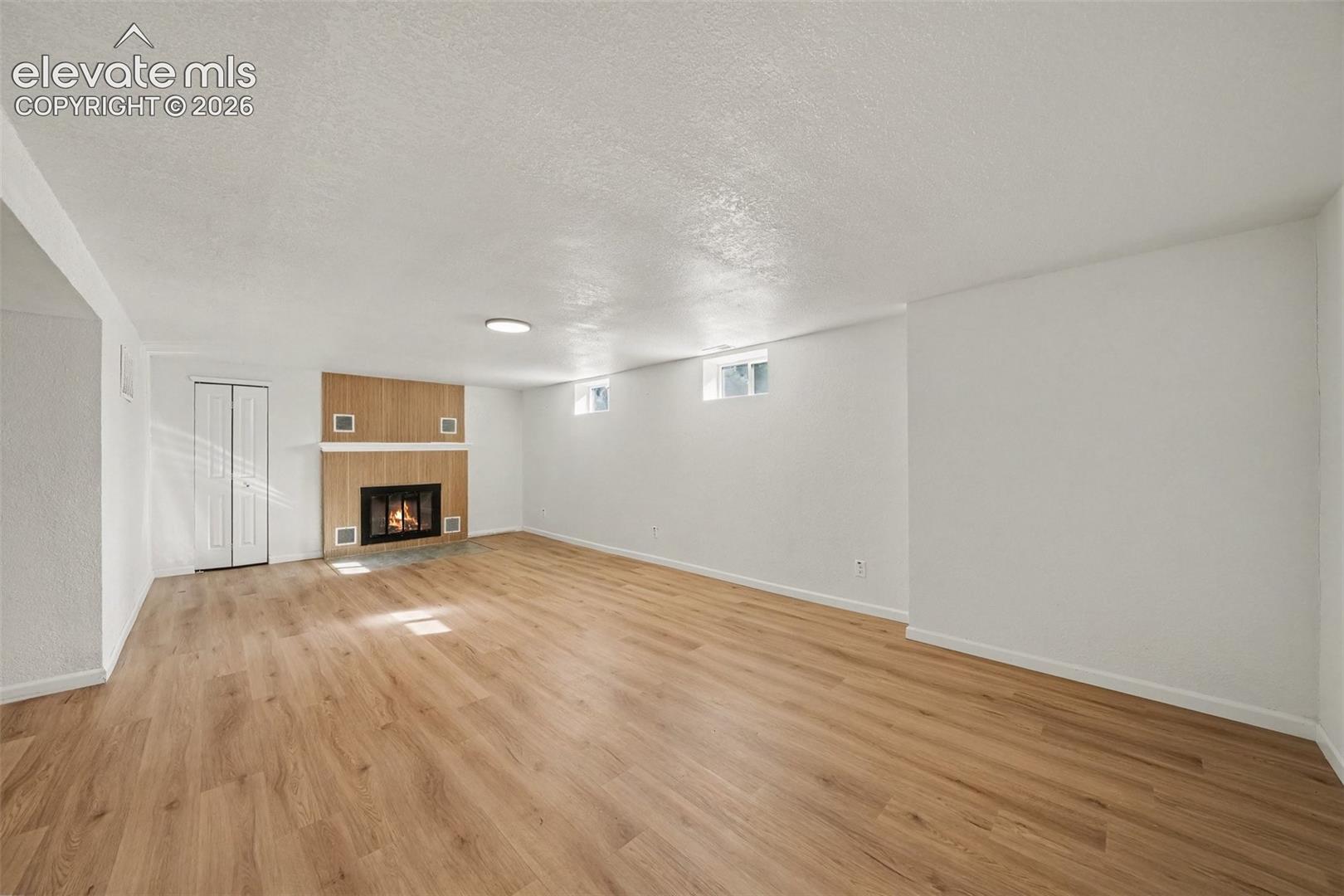 Open-concept space featuring wood-finish flooring, a fireplace with a wood-panel surround, recessed ceiling lighting, and accordion-style closet doors