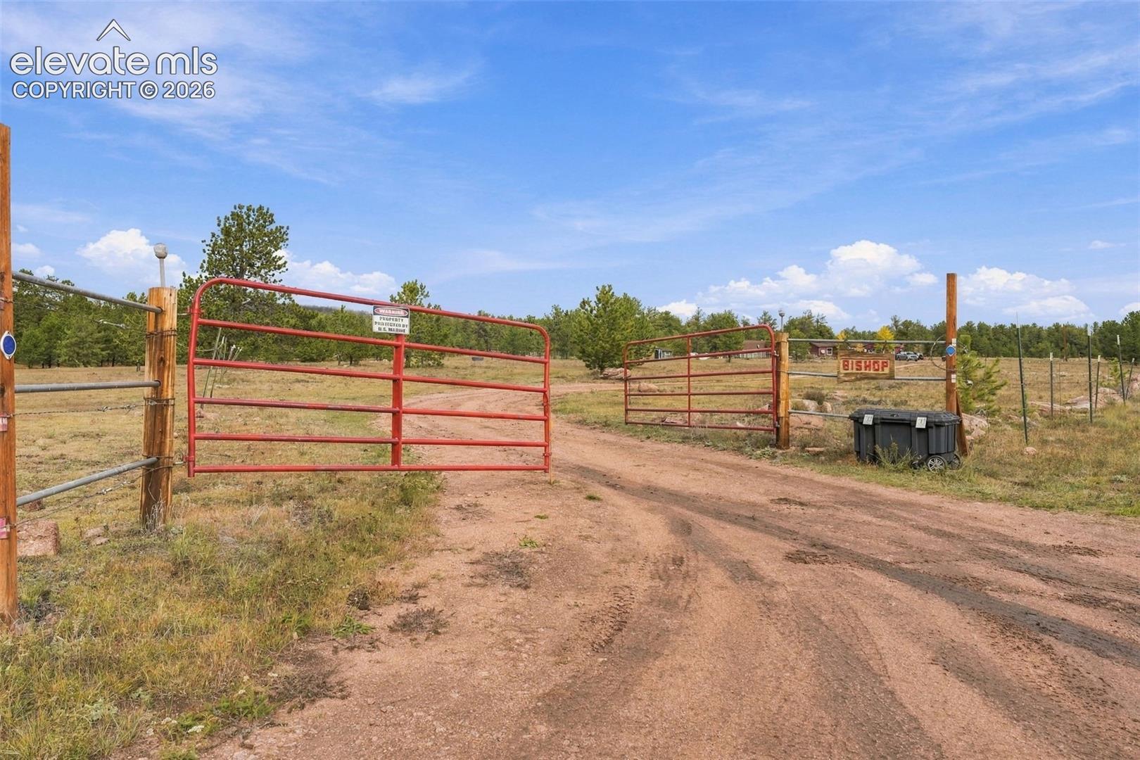 Gated entry featuring heavy-duty red tubular metal swing gates, rugged dirt-surface access road, and perimeter wire fencing