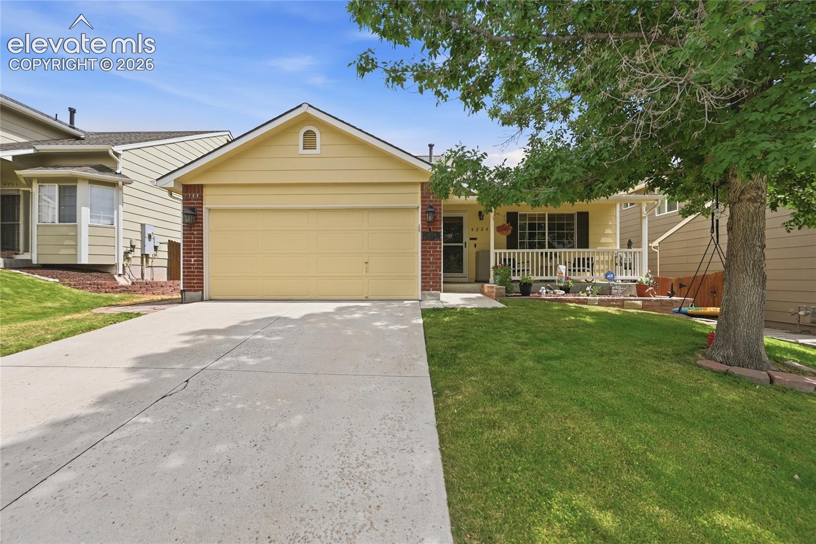 Single-story residence featuring a concrete driveway, two-car garage, brick facade detailing, and a front-facing covered porch with wooden railings