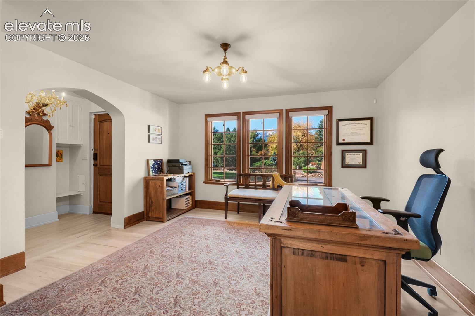 Room featuring wood-finish flooring, a multi-pane window assembly with wood trim, an arched opening to a built-in nook, and a multi-arm chandelier