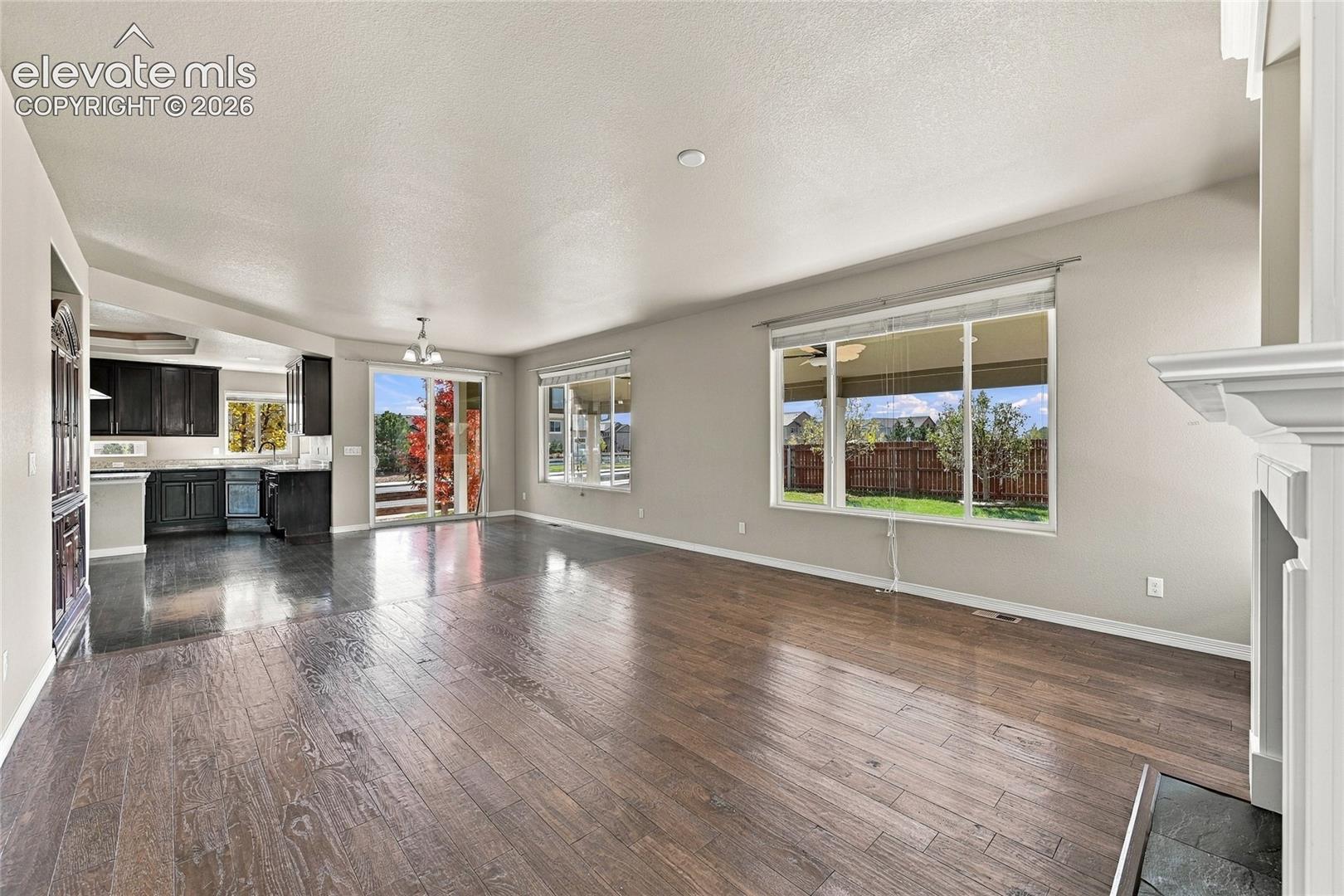 Open-concept interior featuring wood-finish flooring, a white-mantel fireplace, large picture windows, and glass sliding doors