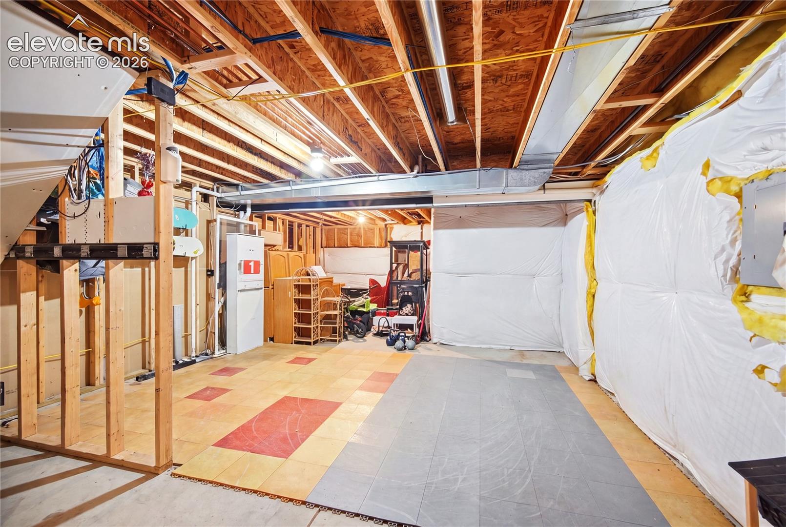 Unfinished lower level featuring exposed wood joist ceilings, HVAC ductwork, insulated wall barriers, and modular flooring tiles