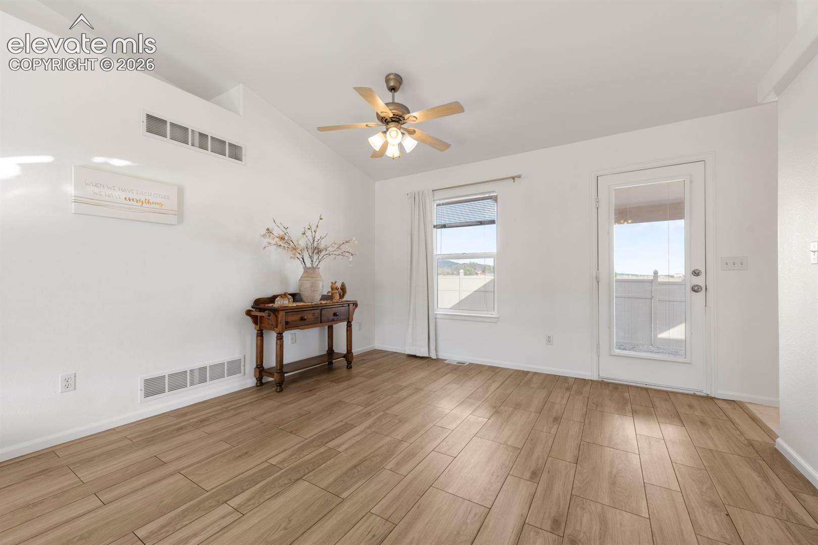 Vaulted ceilings, wood-finish flooring, ceiling fan with integrated lighting, and glass-paneled exterior door