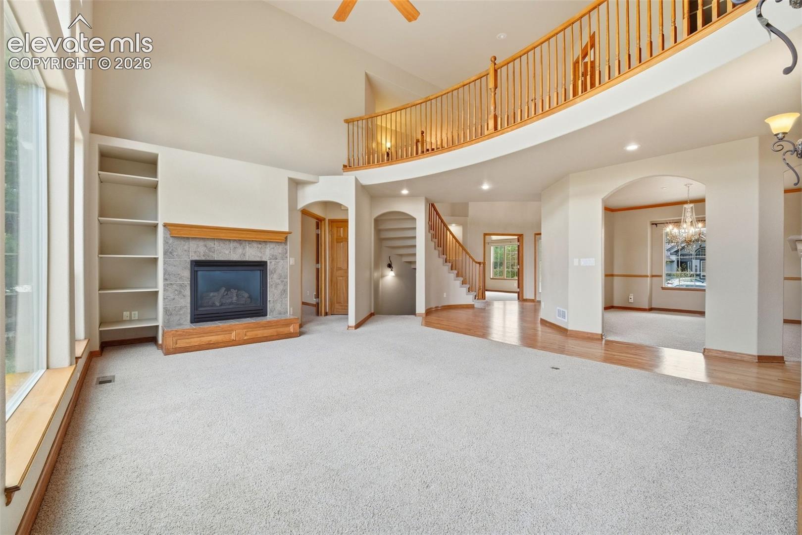 Vaulted ceilings, fireplace with stone surround and wood mantel, built-in shelving, curved wooden staircase railing, and arched architectural entryways