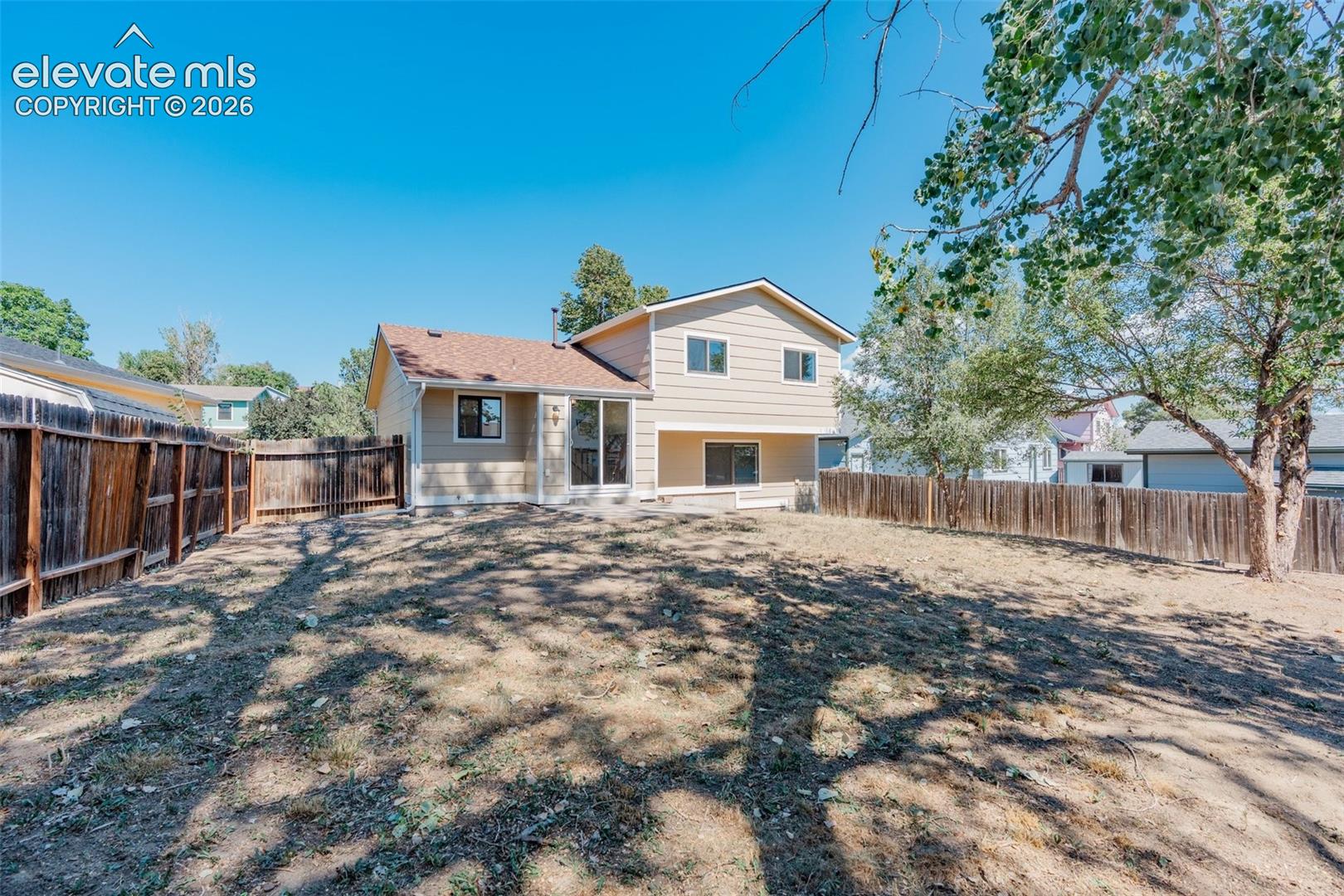 Expansive backyard with a full perimeter fence, mature trees, and a ground-level patio