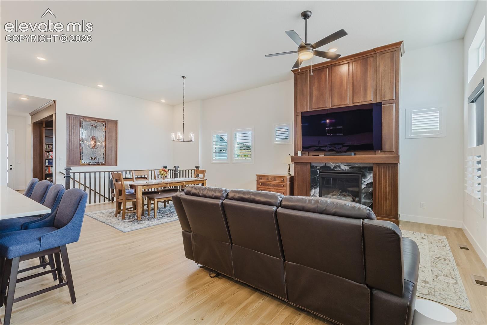 High  ceilings with a ceiling fan, custom wood-built media center that matches the library wood and finish, fireplace and white plantation shutters