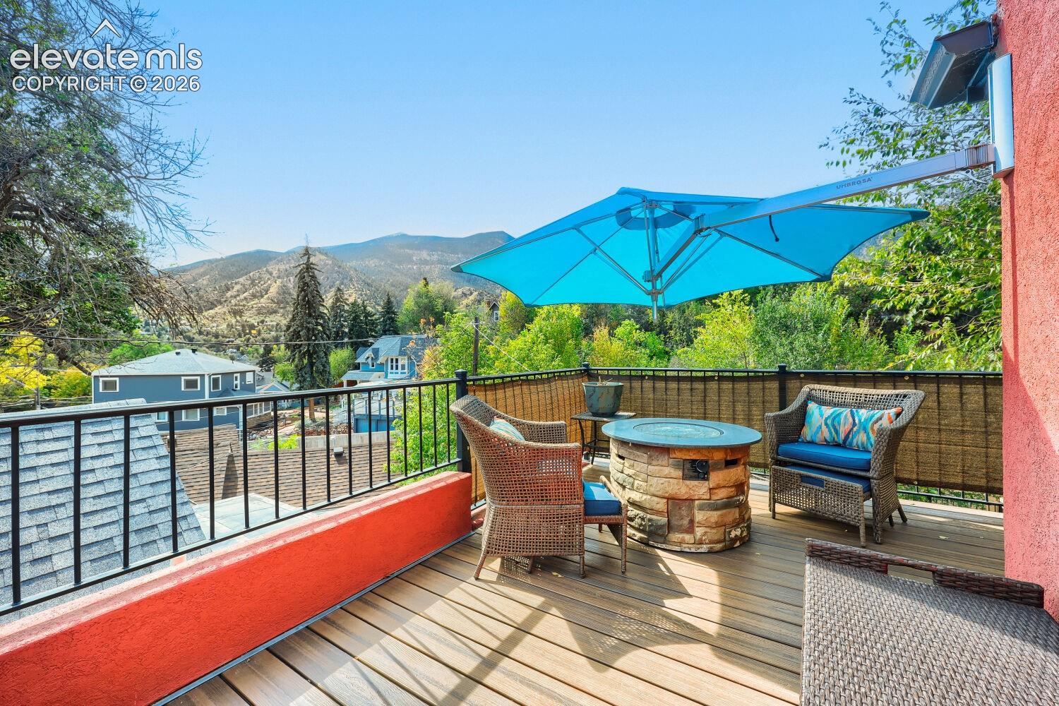 Expansive outdoor deck featuring wood-finish flooring, a stone-clad fire pit, and metal railings