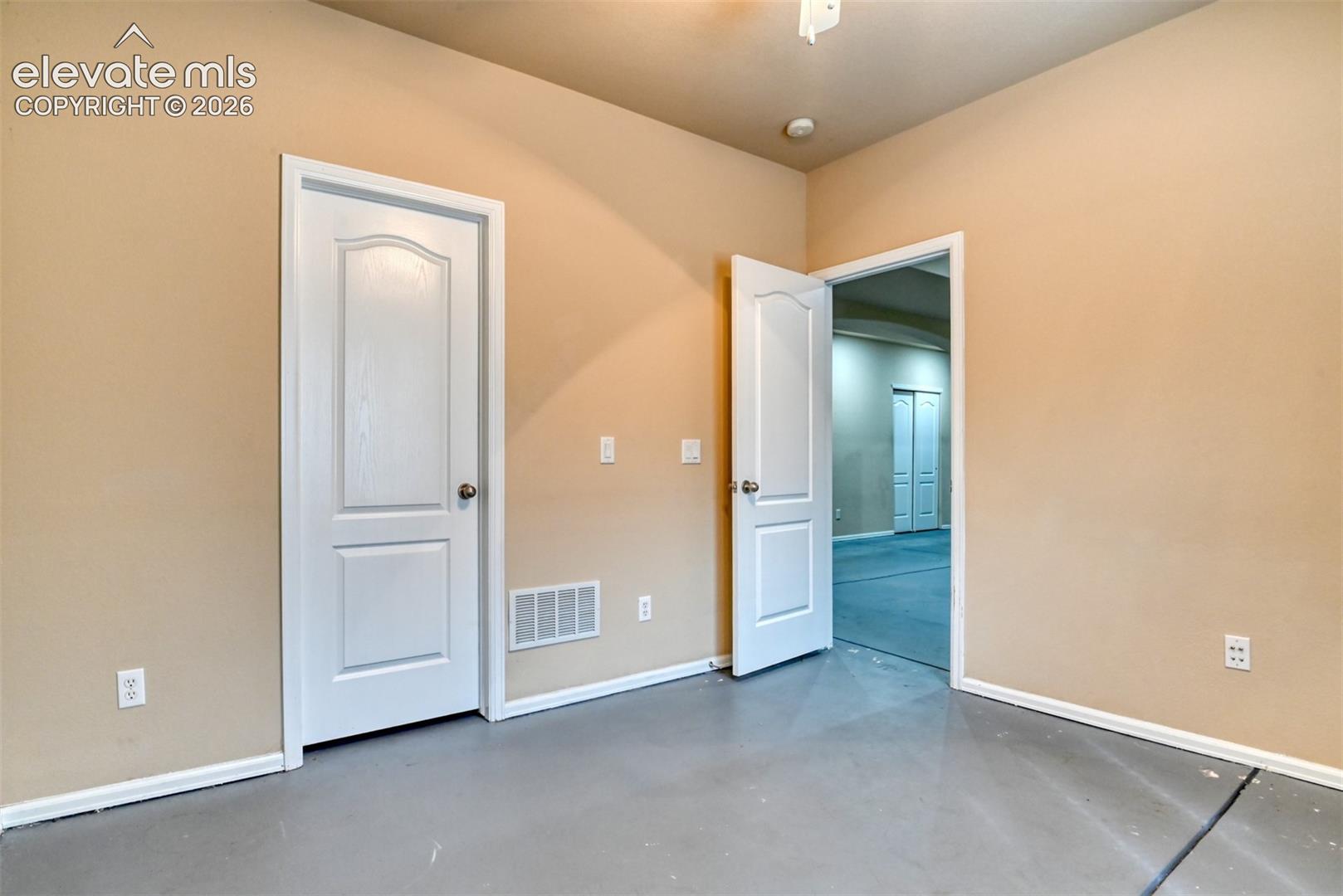 Interior room featuring smooth-finish walls, two-panel arched interior doors with polished hardware, and painted concrete flooring