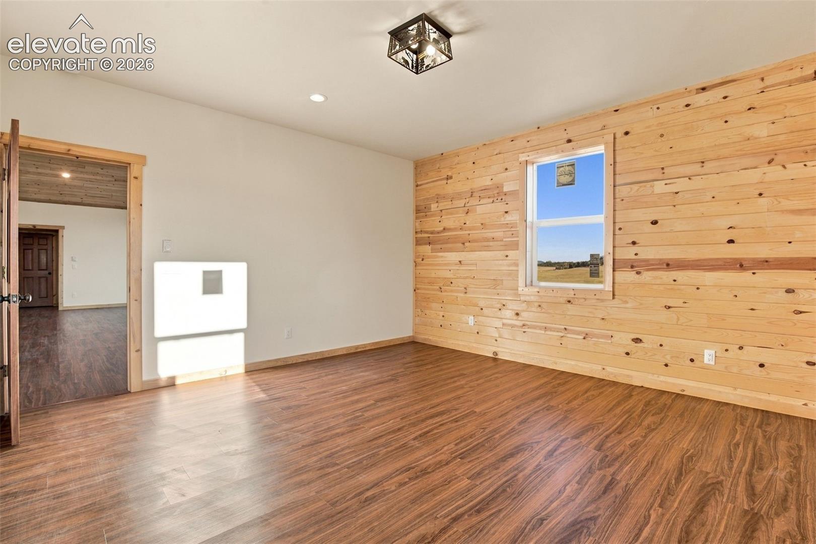 Interior room featuring natural wood-plank wall paneling, wood-finish flooring, a flush-mount geometric ceiling light, and a single-hung window