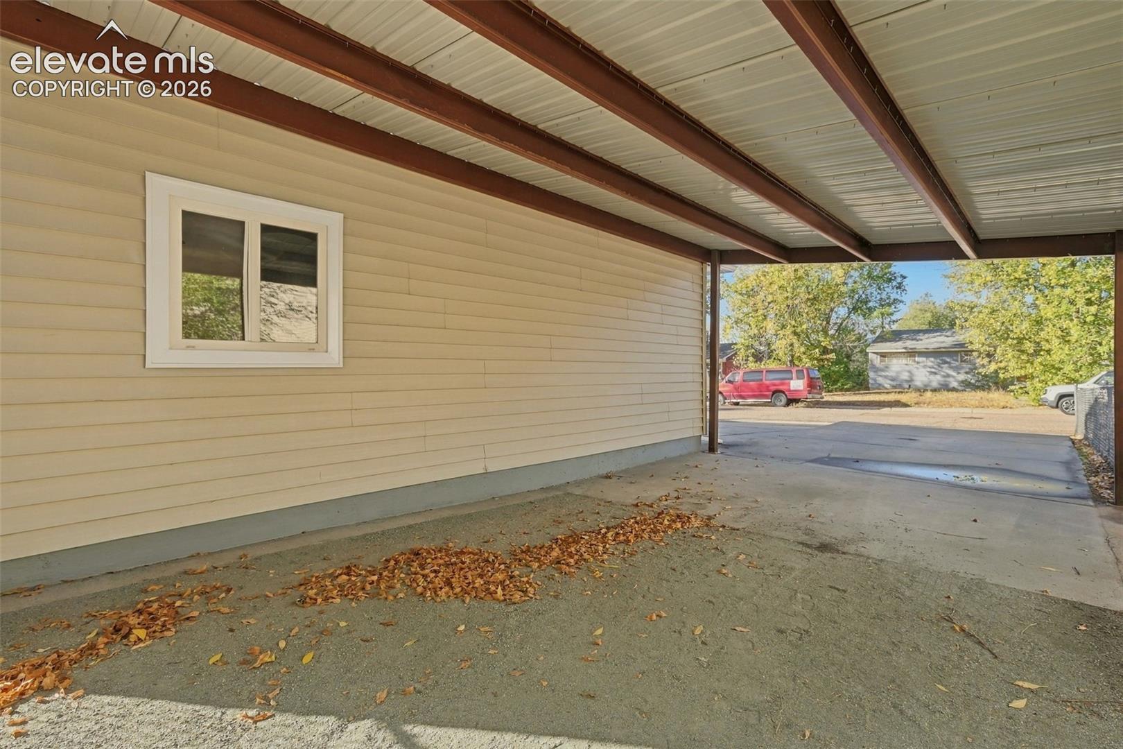 Covered carport featuring metal structural beams, horizontal vinyl siding, and concrete paving