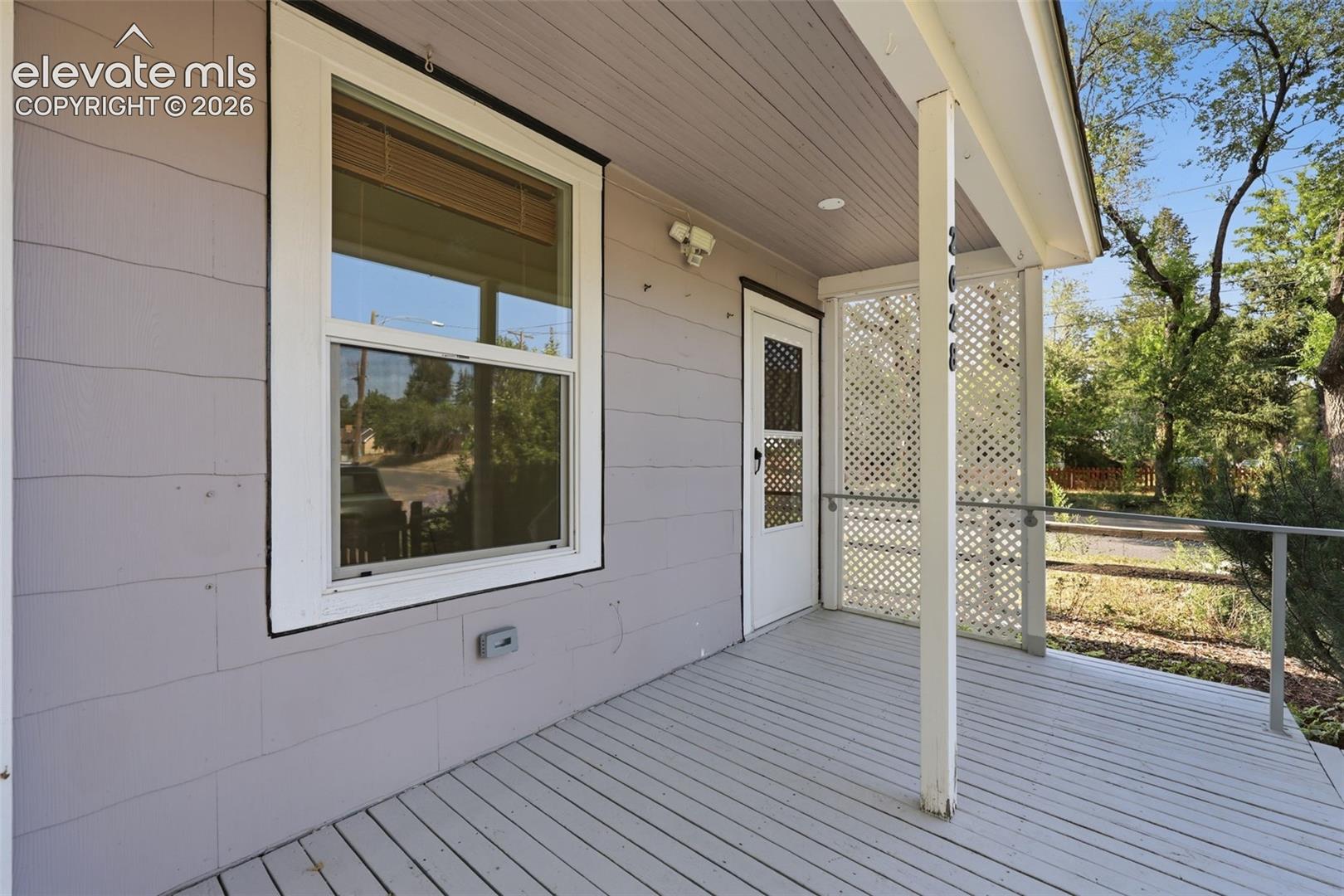 Front porch with wood decking, white lattice privacy screen, and white railing.