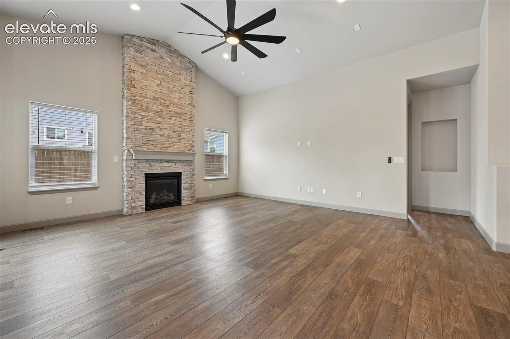 Vaulted ceilings, floor-to-ceiling stone-veneer fireplace, wood-finish flooring, recessed lighting, and built-in wall niche