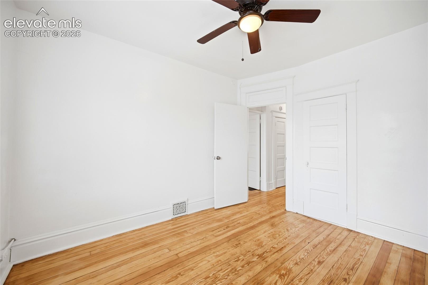 Wood-finish flooring, five-panel interior door, millwork door casing, and a ceiling-mounted light fixture with fan blades