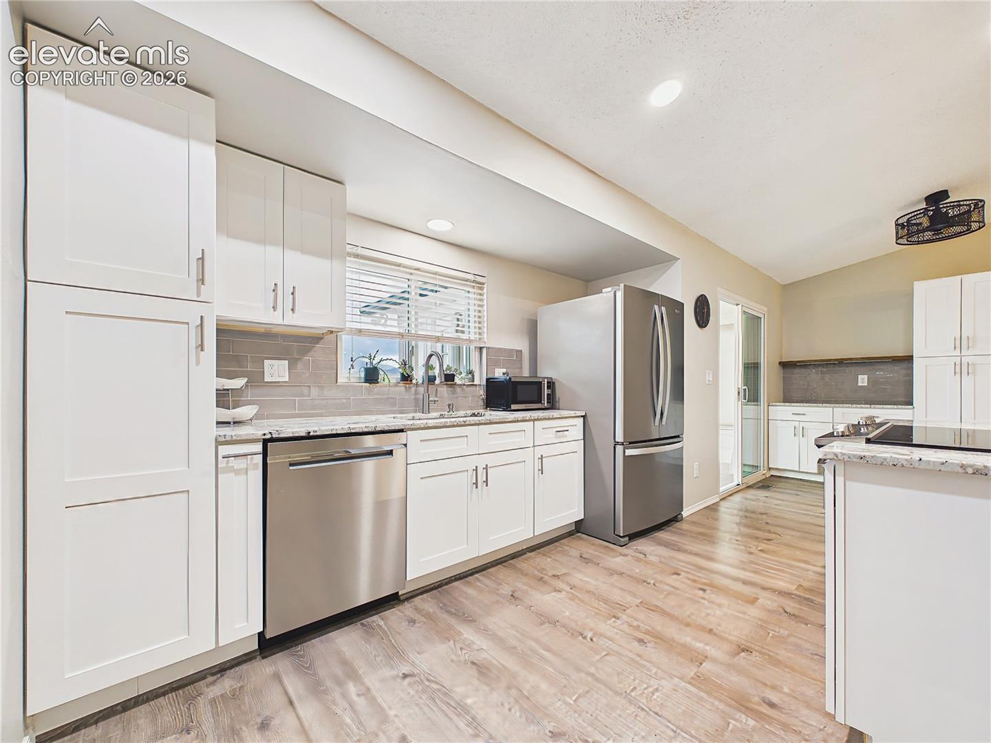 Beautifully updated kitchen featuring white shaker cabinetry, granite countertops, stainless steel appliances, subway tile backsplash, and abundant natural light.