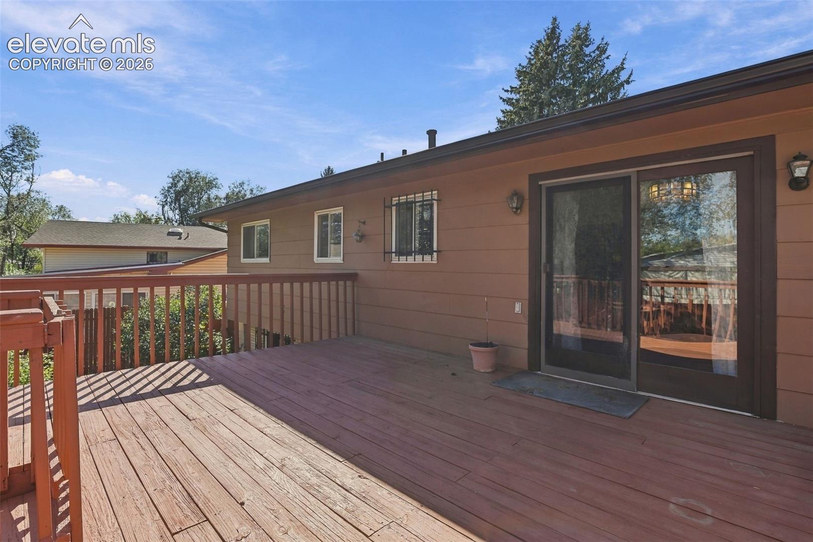Expansive wood deck with a matching railing, horizontal exterior siding, sliding glass door, and wall-mounted exterior lighting