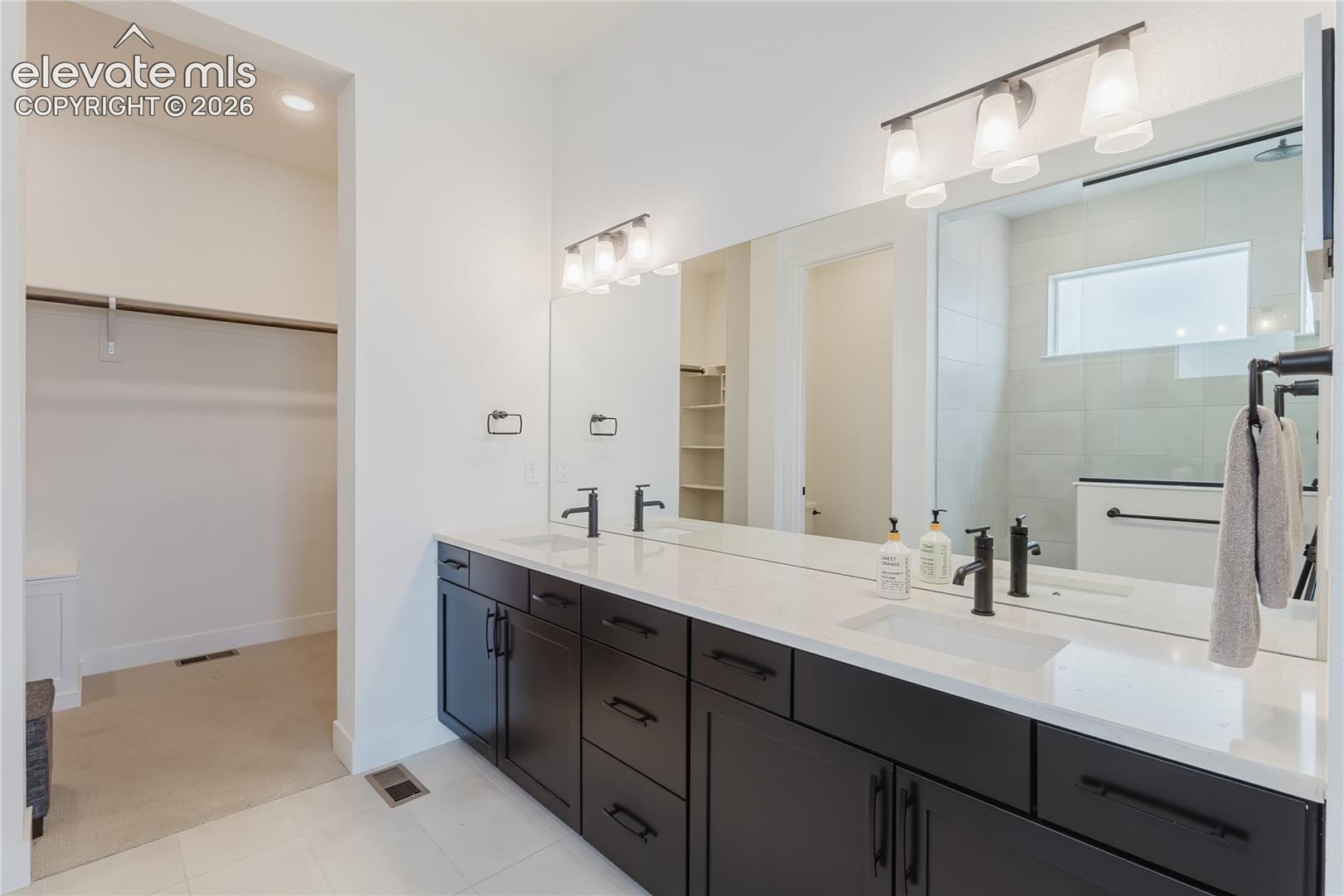 Dual vanity with white countertop, dark wood-finish cabinetry, and black fixtures.  Note the white fixture in the closet is a laundry pass through to the utility room 