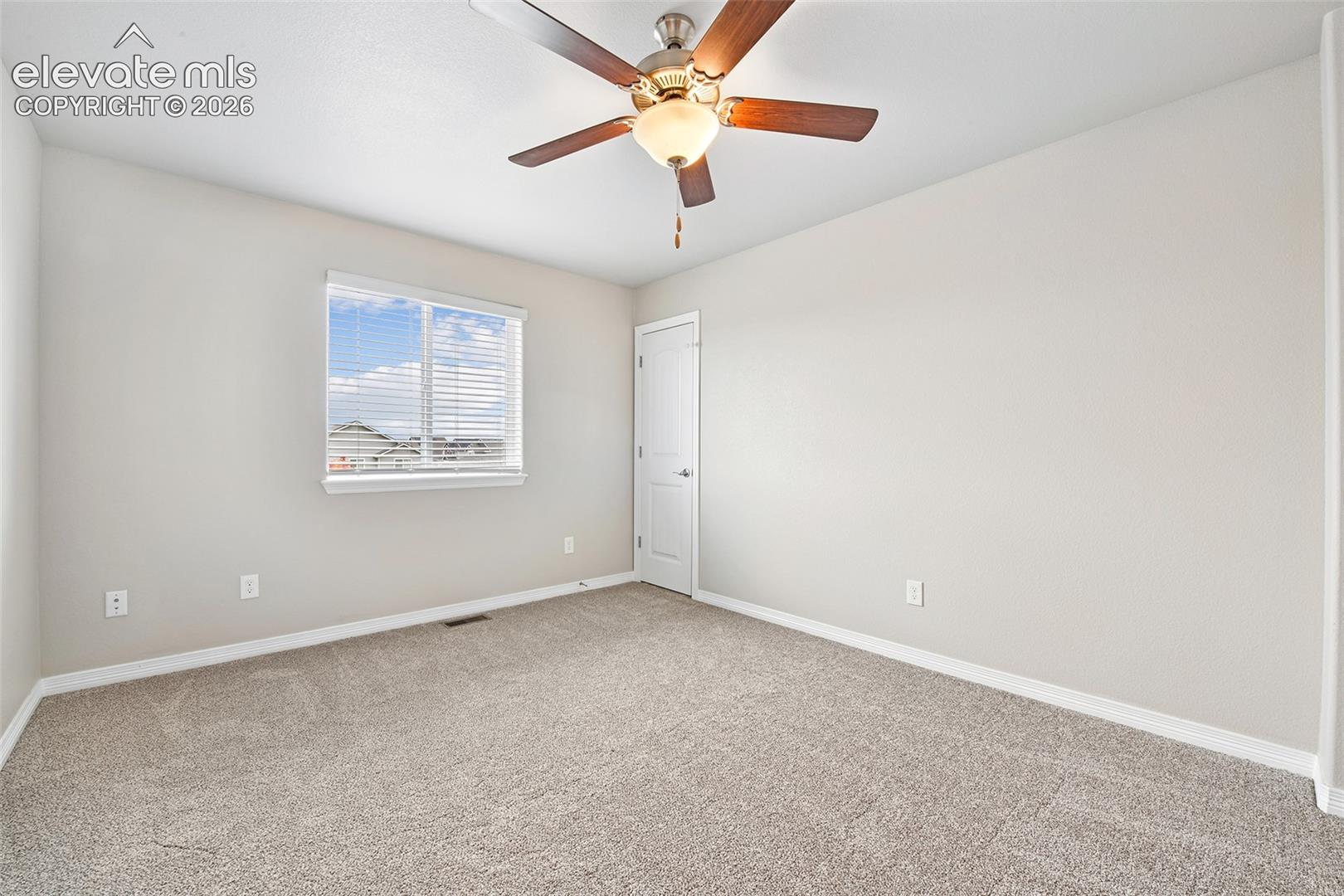 Neutral-toned interior room featuring wall-to-wall carpeting, a multi-blade ceiling fan with integrated lighting, and a single-panel interior door