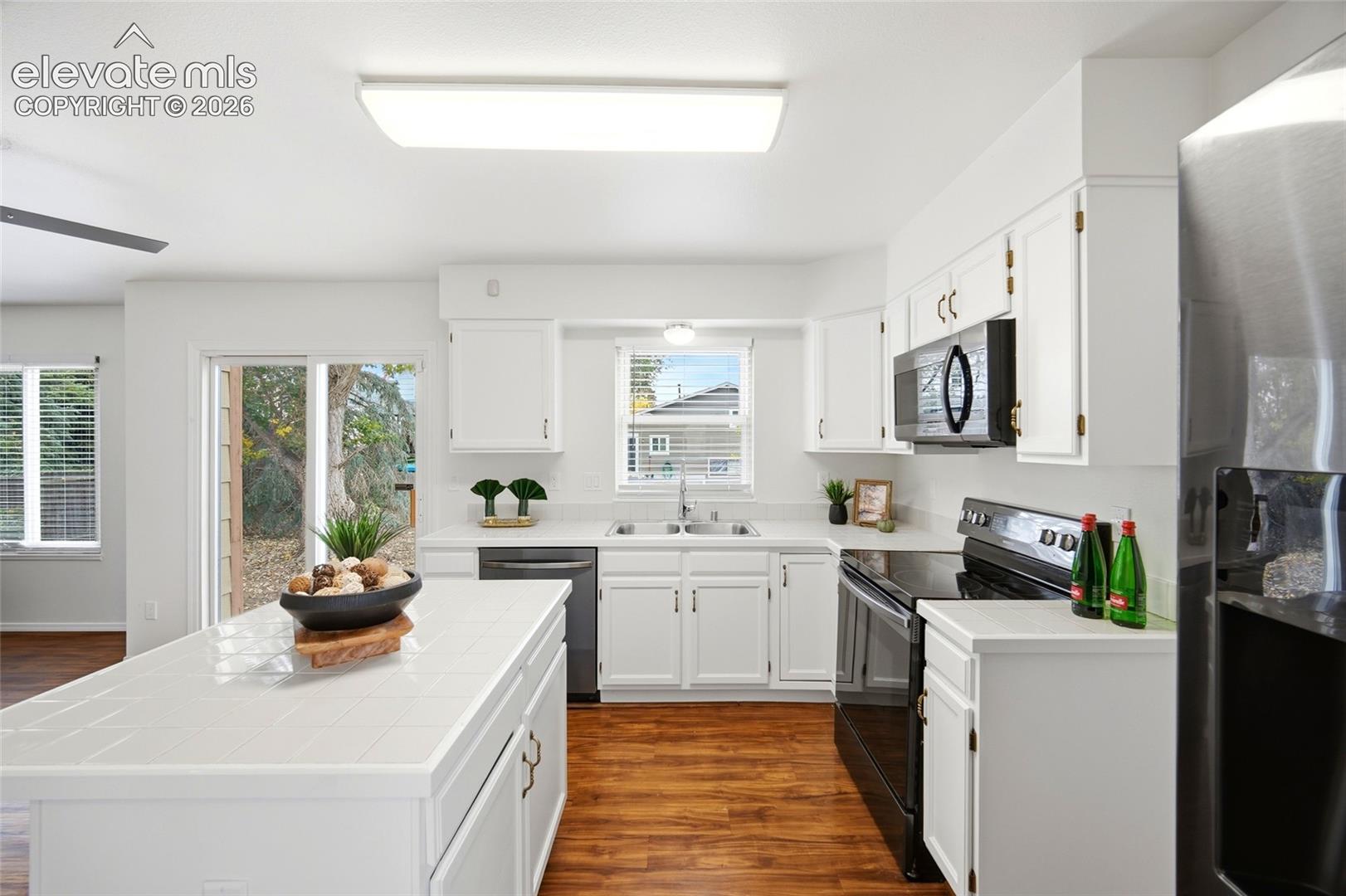 Kitchen featuring white cabinetry, a central island with a tiled countertop, wood-finish flooring, and black appliances
