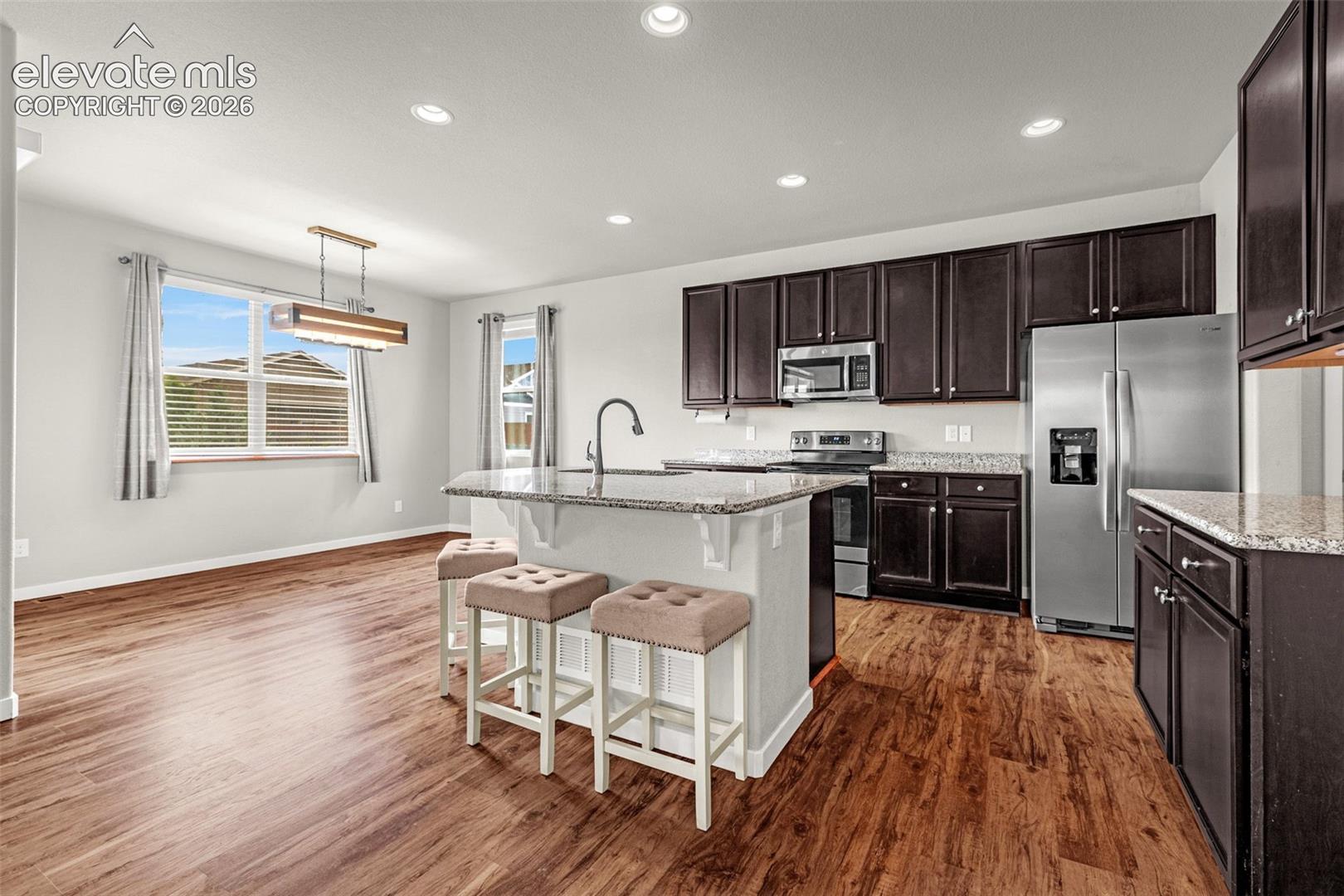 Kitchen featuring dark wood-finish cabinetry, stainless steel appliances, and a central island with a sink and stone-finish countertop