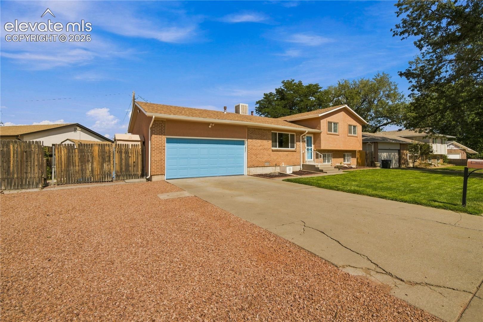 Brick and stucco exterior with a light blue garage door, concrete driveway, and gravel parking area