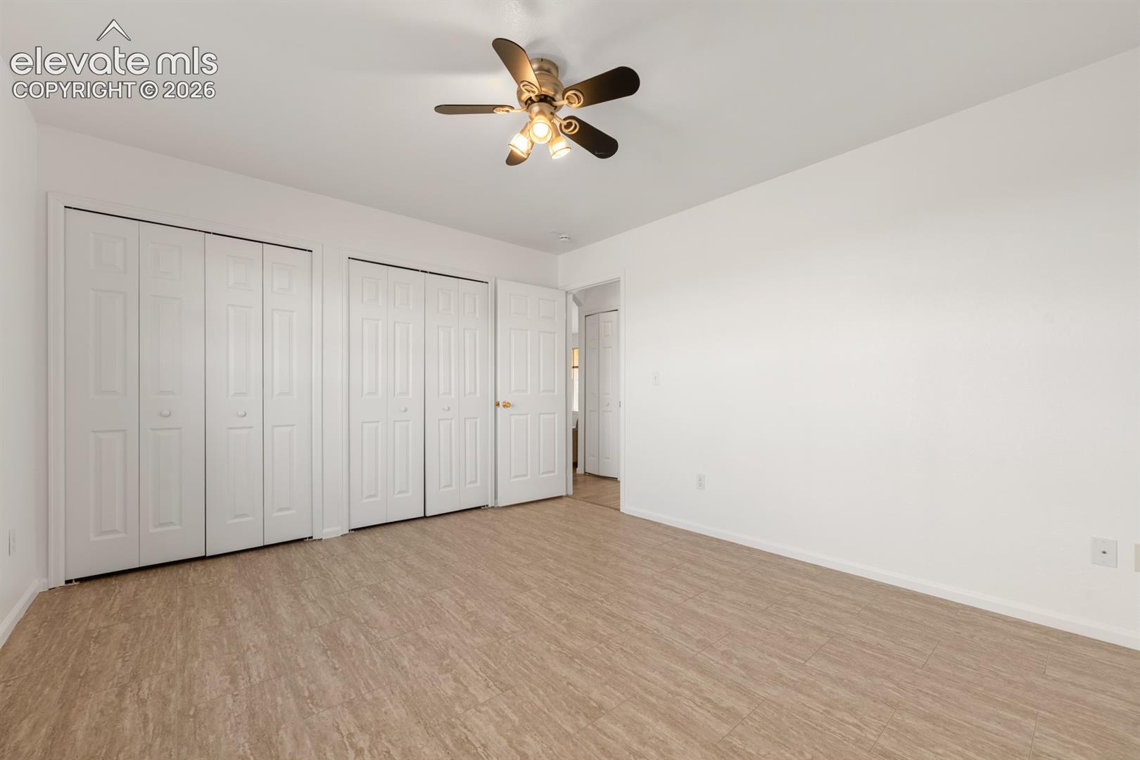 Room featuring wood-finish flooring, dual bi-fold door closets, and a ceiling-mounted light fixture with a fan