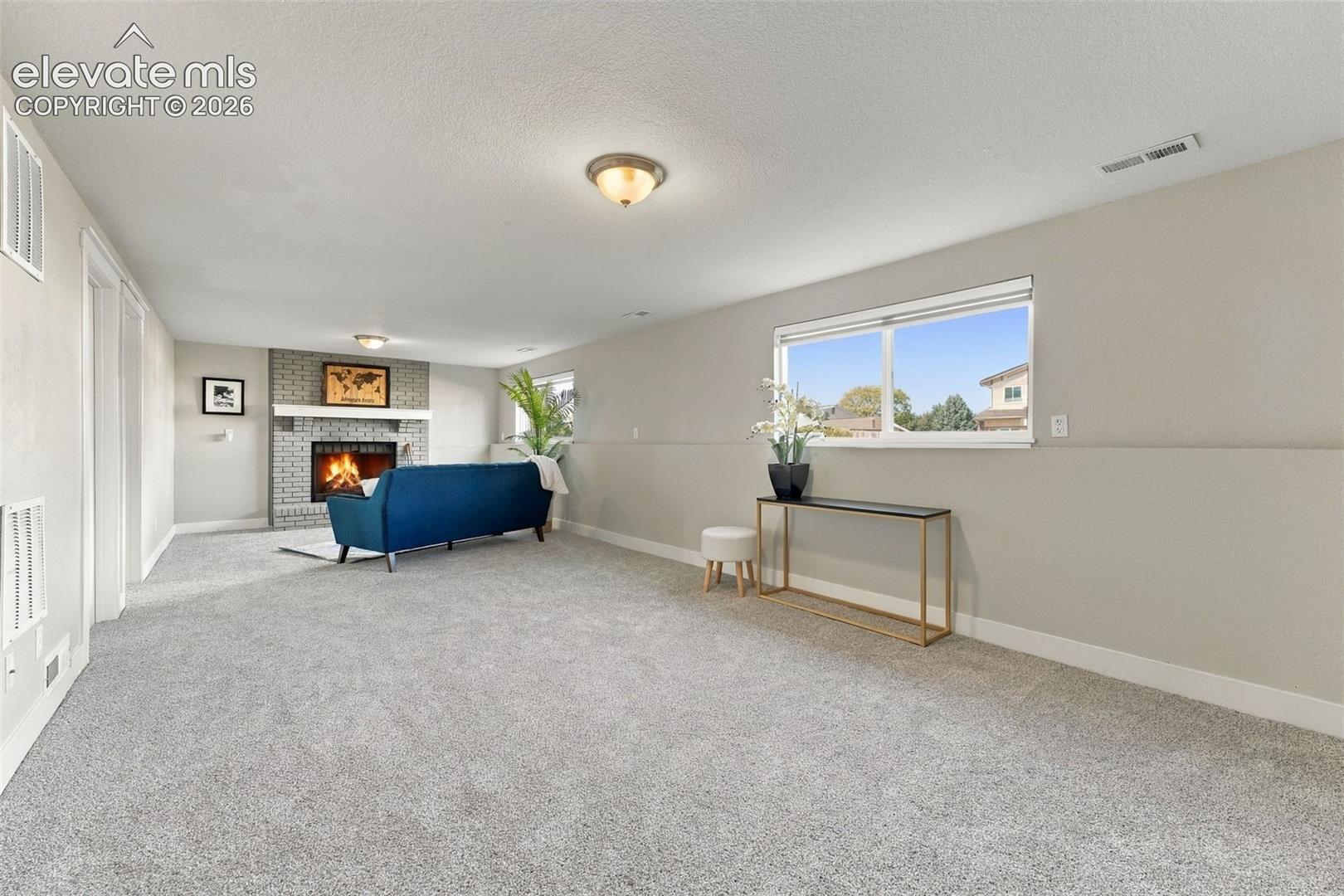 Spacious room featuring light-colored carpeting, a brick-surround fireplace with a white mantel, and a window providing natural light